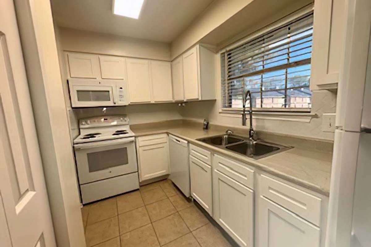 Modern kitchen featuring white cabinetry, a stainless steel sink with a double basin, a microwave and oven combo, and a refrigerator. The room has beige tile flooring and a window allowing natural light to illuminate the space.