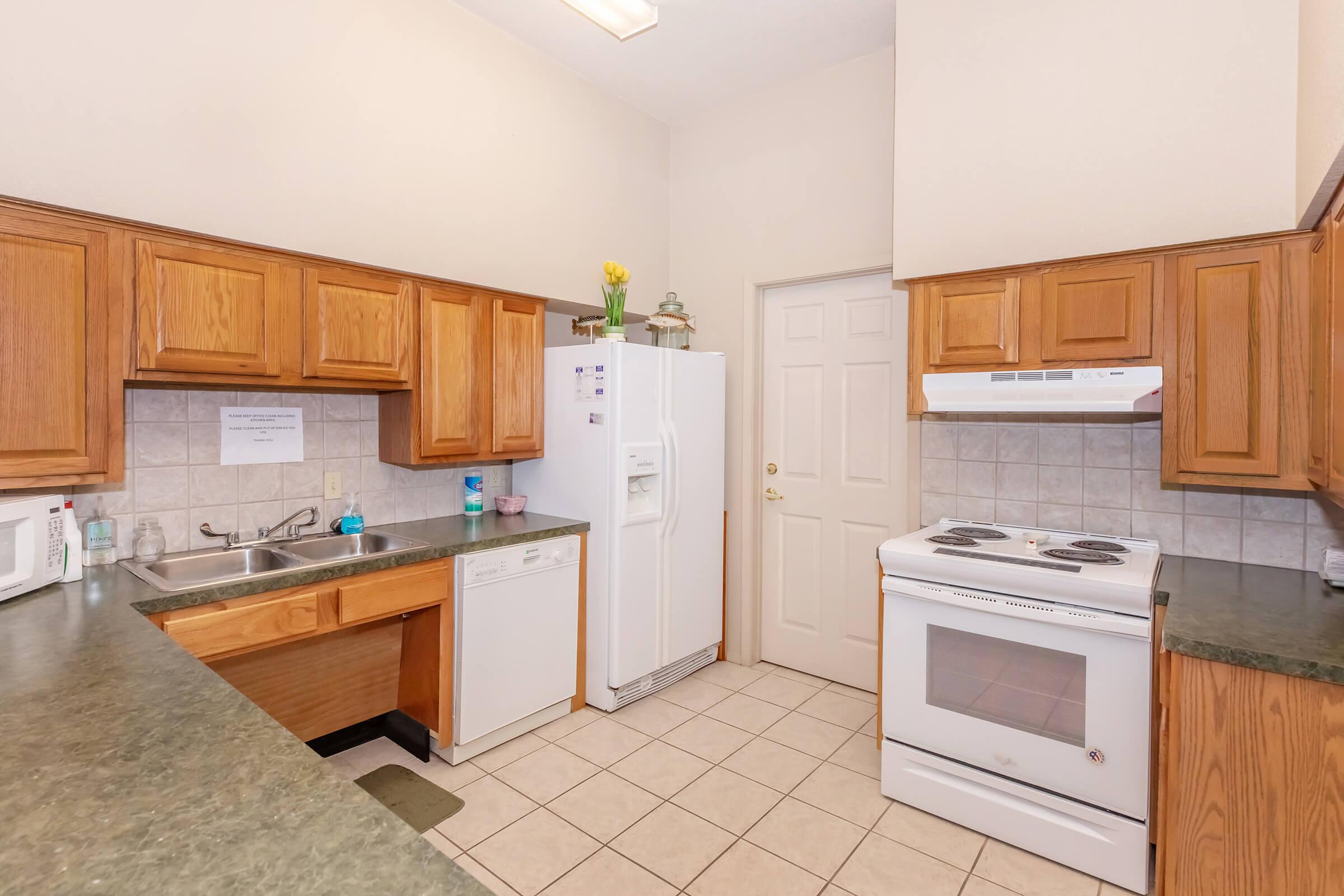 Modern kitchen with wooden cabinets, a white refrigerator, and a stove. The space features a tiled floor, a stainless steel sink, and a dishwasher. Natural light fills the room, highlighting the organized countertops.