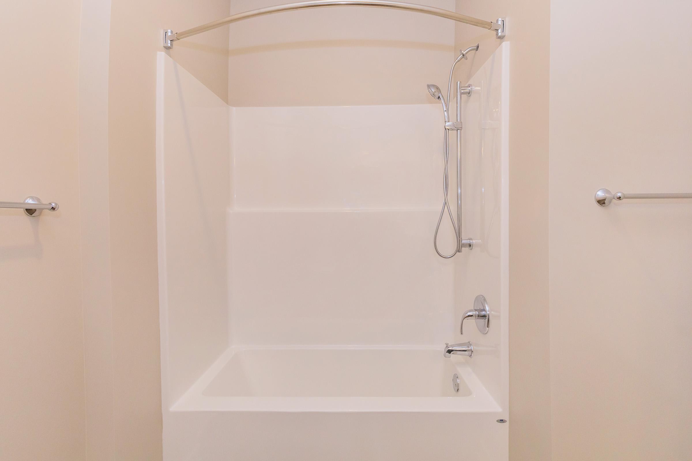 A clean, modern bathtub and shower enclosure with a curved shower rod and adjustable showerhead, set against neutral-colored walls. The space appears well lit and minimalistic, ideal for a contemporary bathroom design.