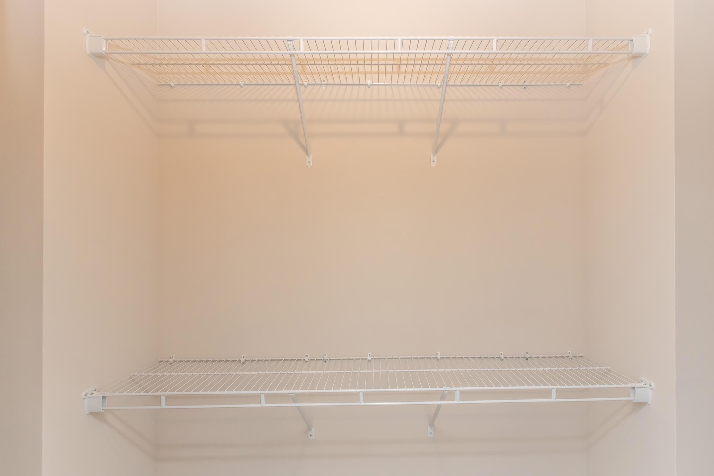 Empty wire shelving units mounted on a light-colored wall, featuring two horizontal shelves with a simple, open design, ideal for storage and organization. The top shelf has three dividers, while the bottom shelf is flat and unobstructed, creating a clean and minimalist look.
