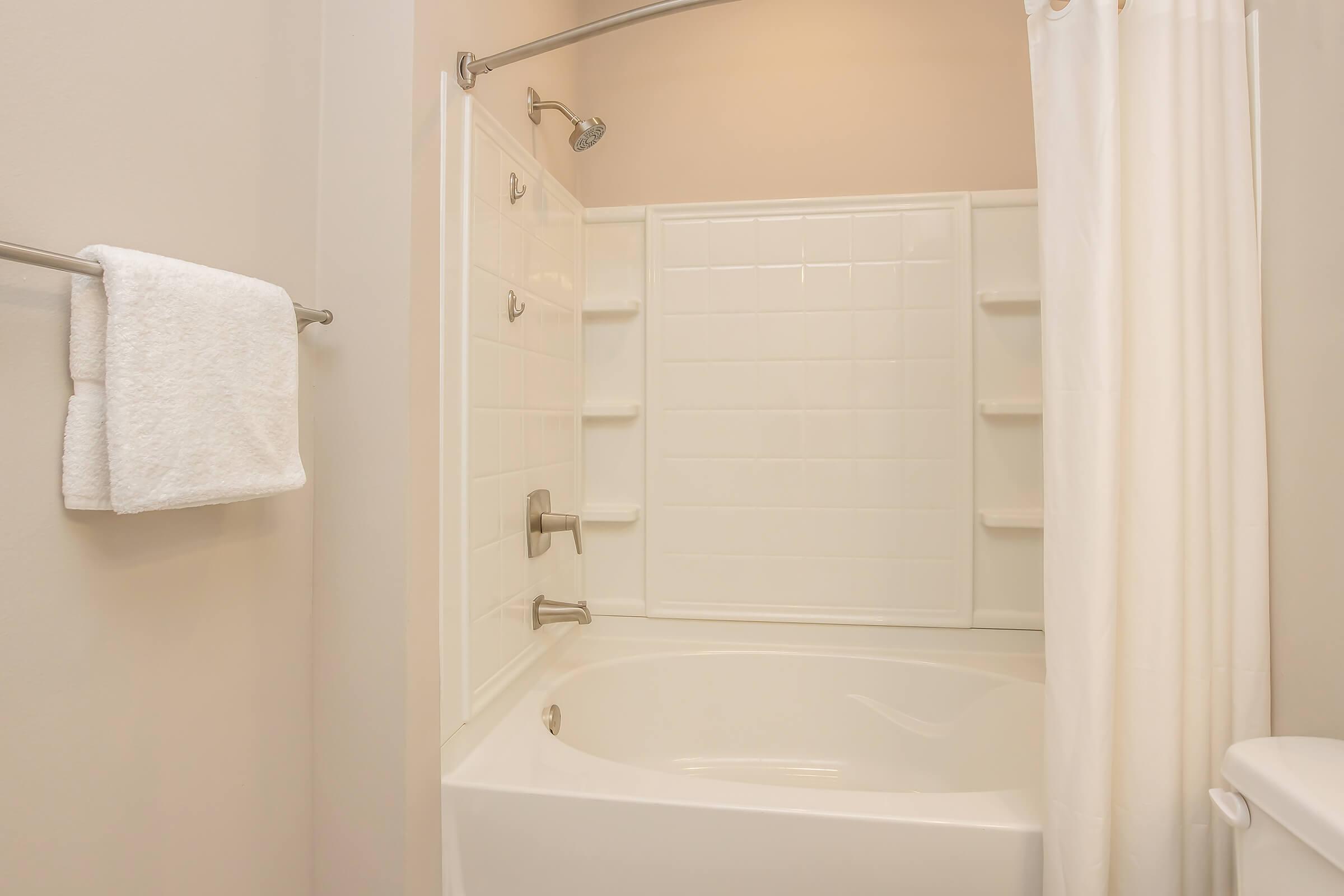 A clean and modern bathroom featuring a white shower tub combo, a wall-mounted towel rack with a white towel, and a shower curtain. The walls are painted in a neutral tone, and the space is well-lit, creating a bright and inviting atmosphere.