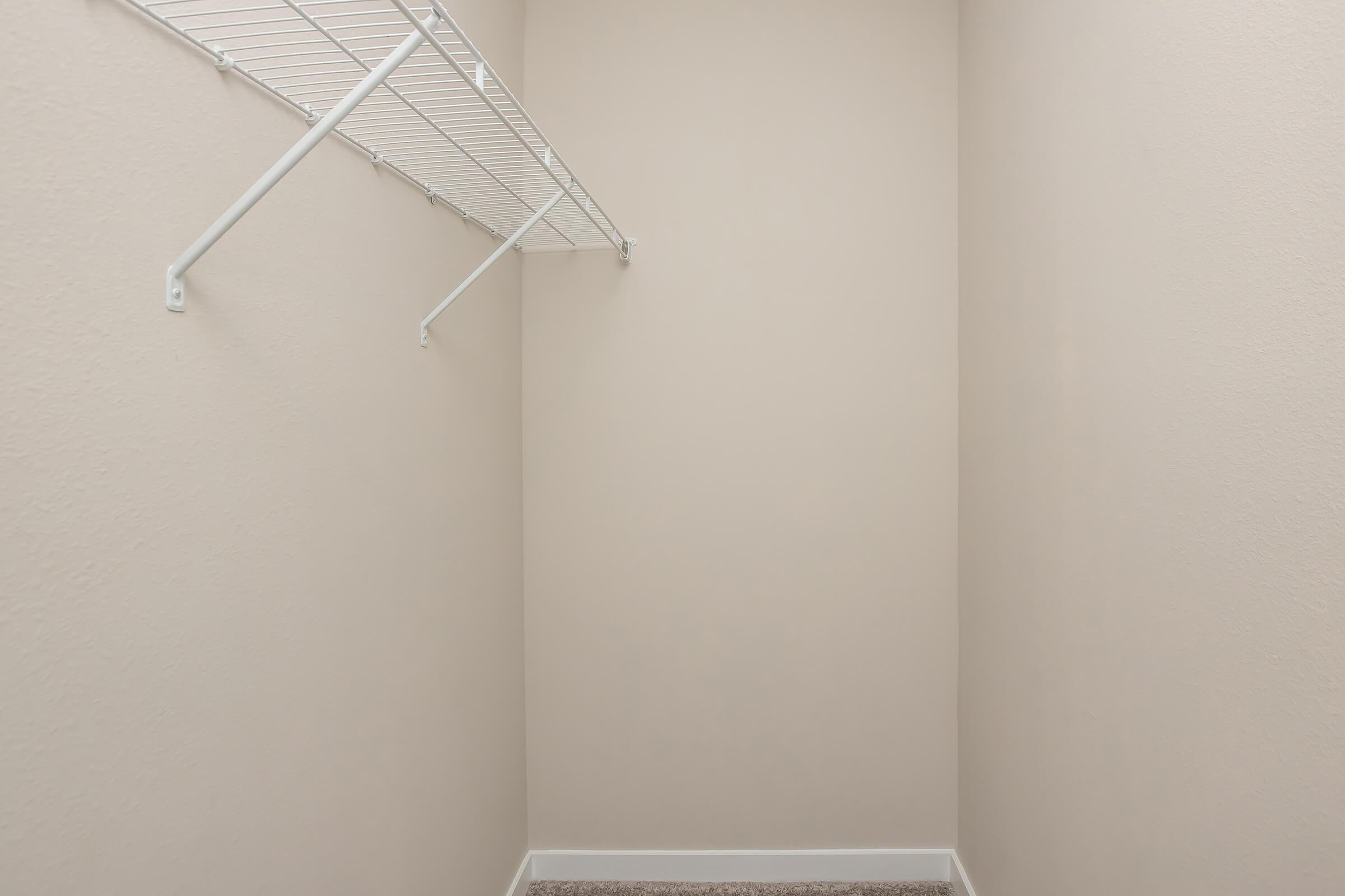 Empty closet with light beige walls, featuring a white wire shelf mounted on one side. The floor is covered with carpet, and there are no items or furniture inside the space, creating a clean and minimalistic appearance.