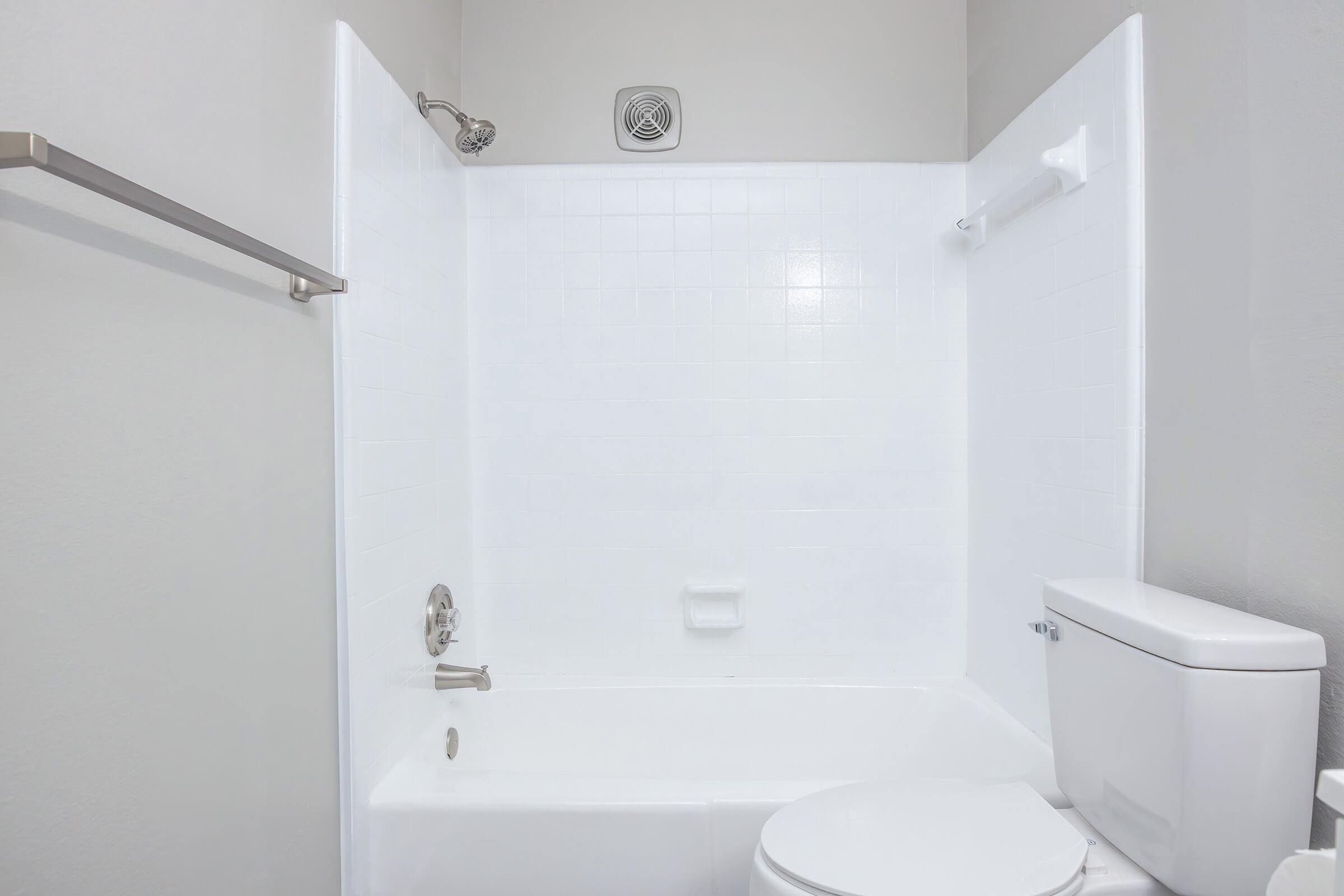 A clean, modern bathroom featuring a white bathtub and shower combination, a toilet, and a small wall-mounted towel rack. The walls are painted in a light color, and the bathroom has a simple and uncluttered design. Light is bright, enhancing the fresh appearance of the space.