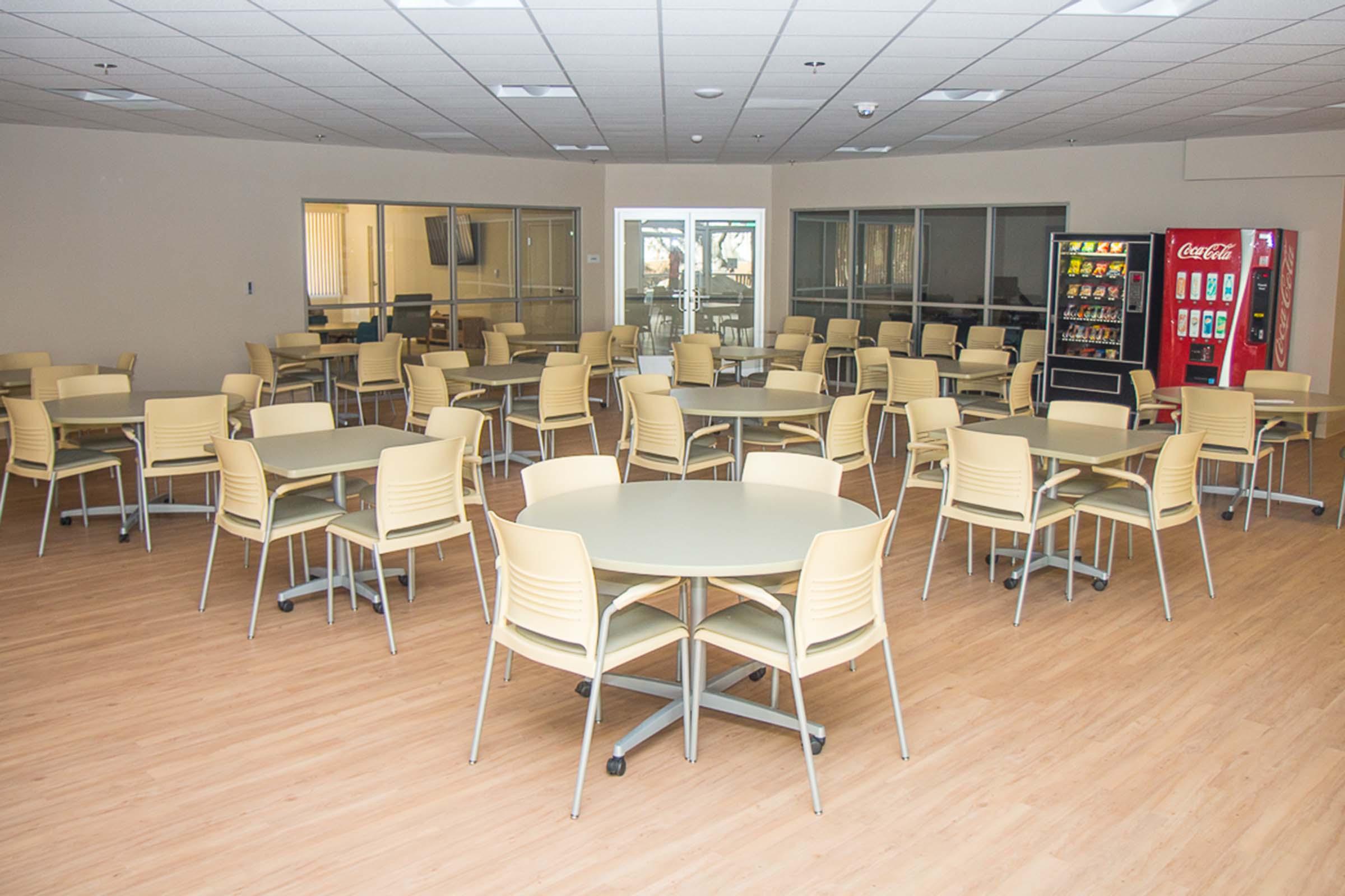 Community room with tables and chairs, with vending machines in background.