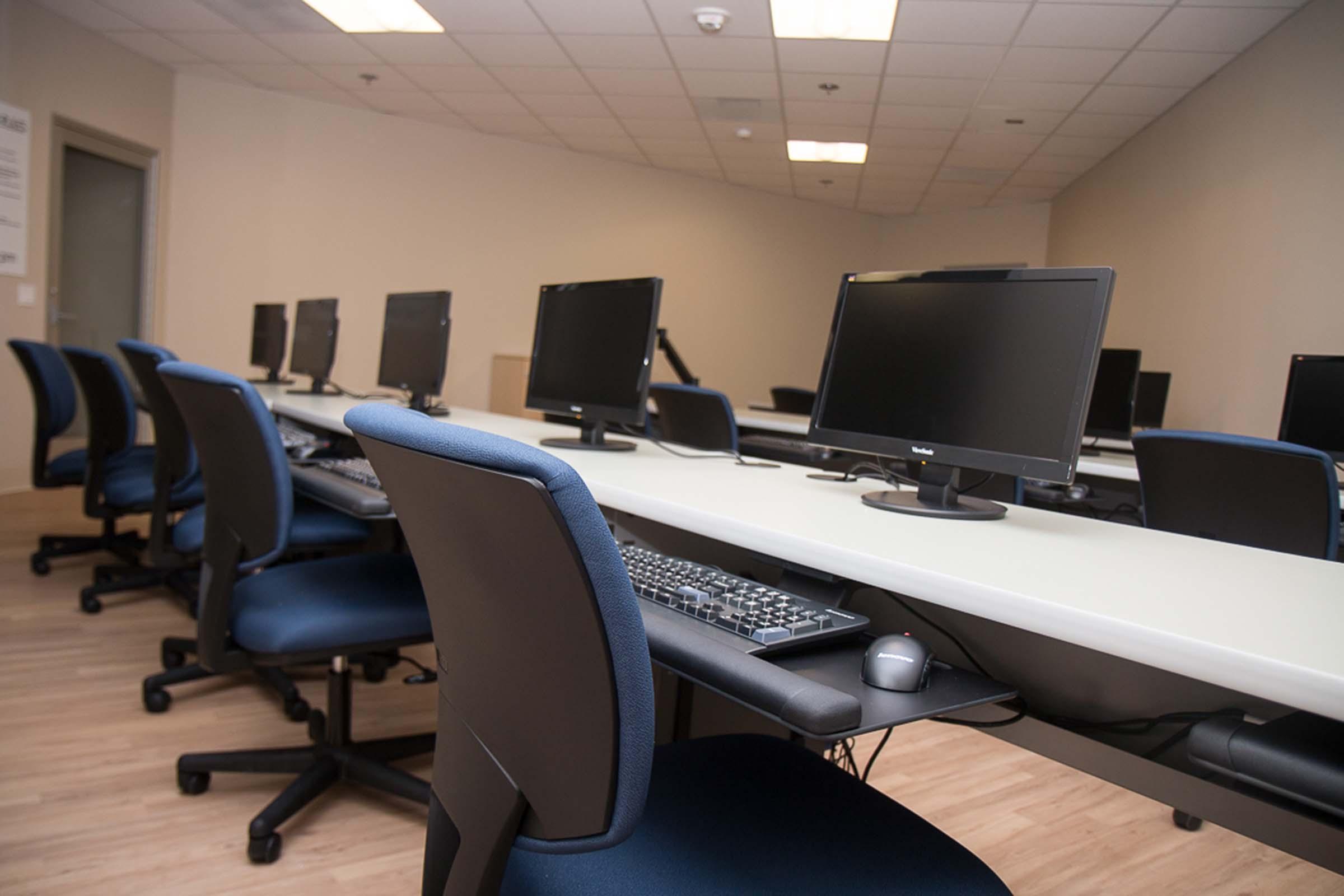 Computer lab with monitors on desks and chairs.