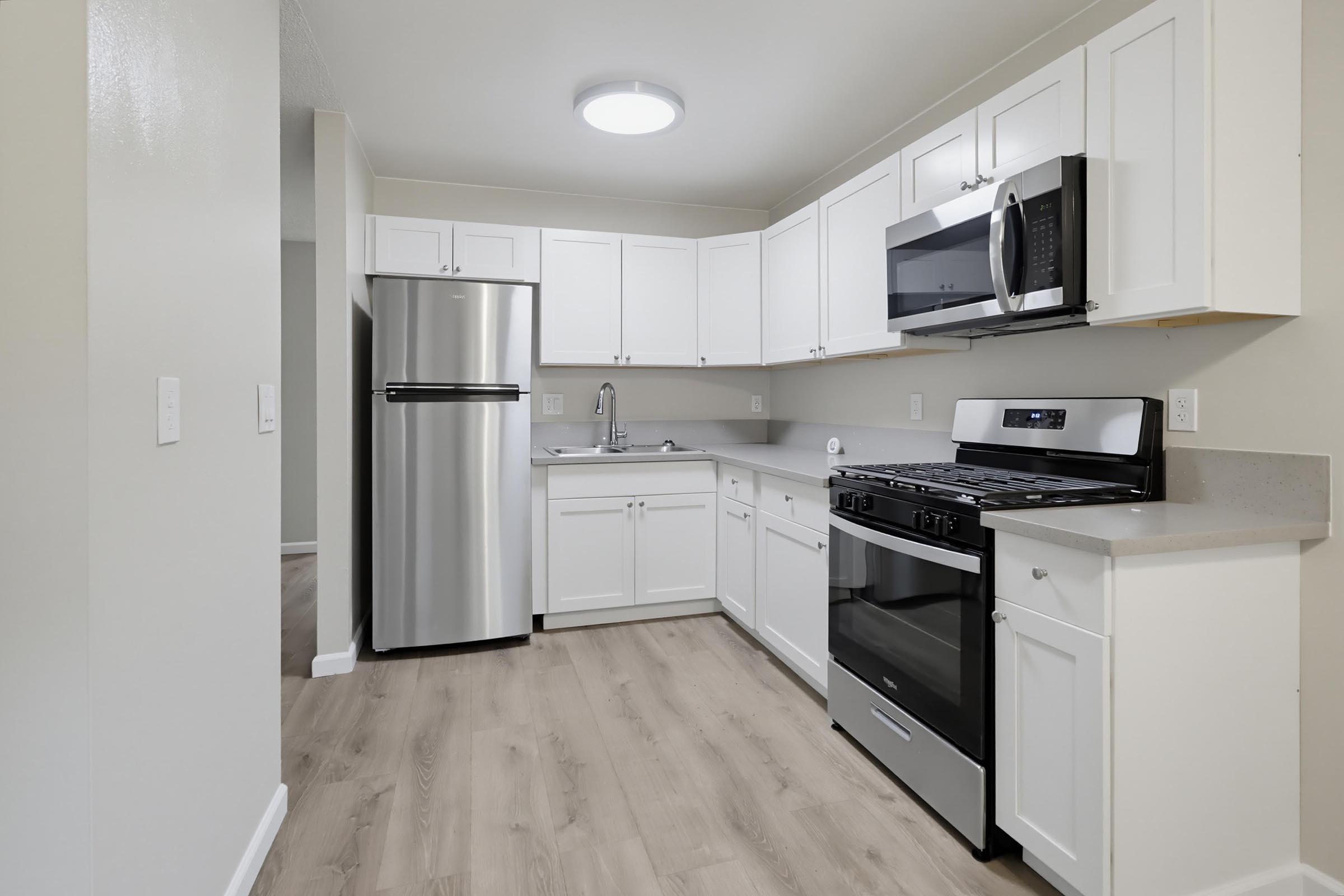 Stylish modern kitchen featuring white cabinetry, stainless steel appliances including a refrigerator and stove, granite-like countertops, and a sleek microwave. The space is bright with natural light and has light wood flooring, creating a contemporary and inviting atmosphere.