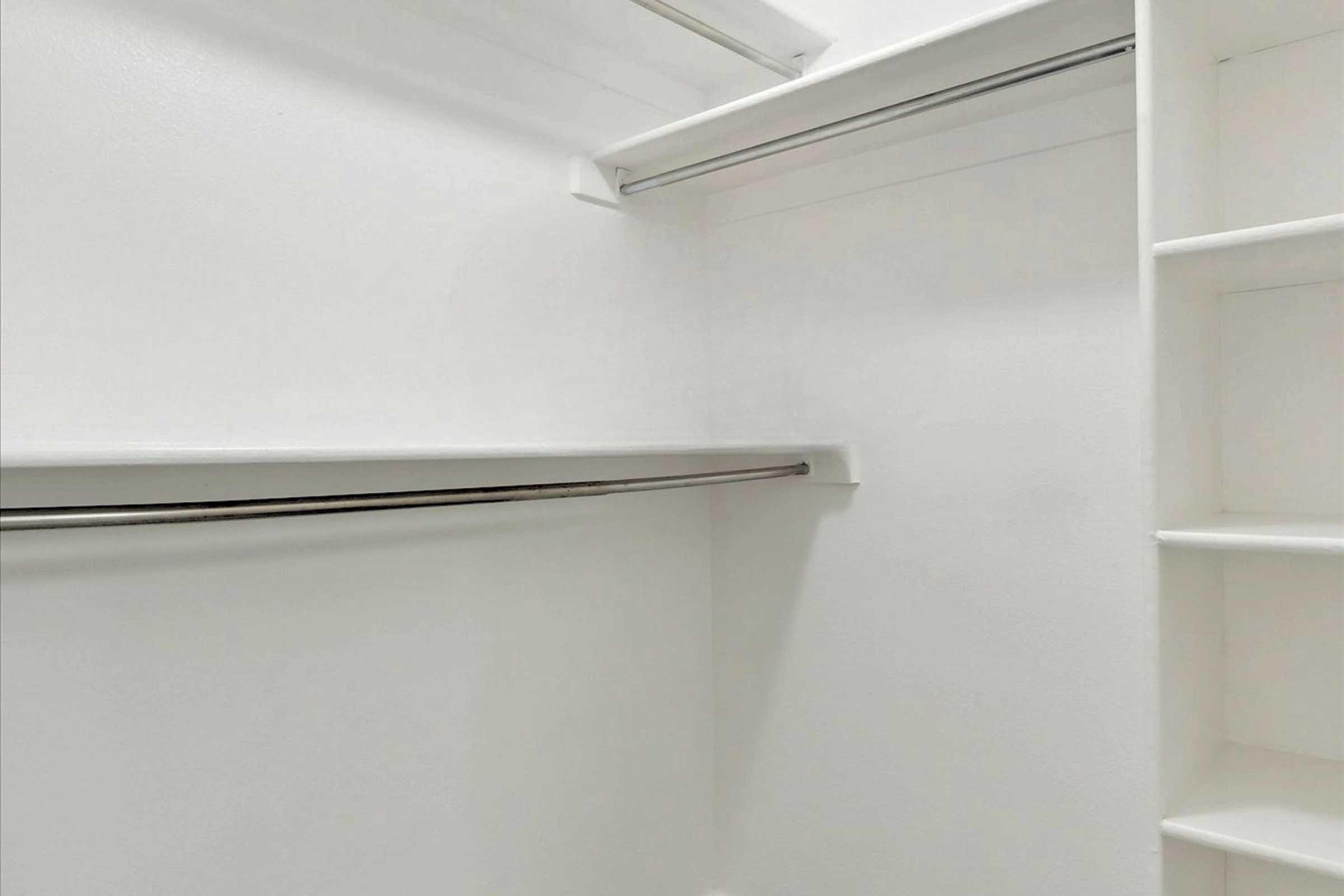 A clean, empty closet featuring white walls, a metal hanging rod, and built-in shelving on one side. The space is well-lit and organized, with a minimalistic design allowing for ample storage.