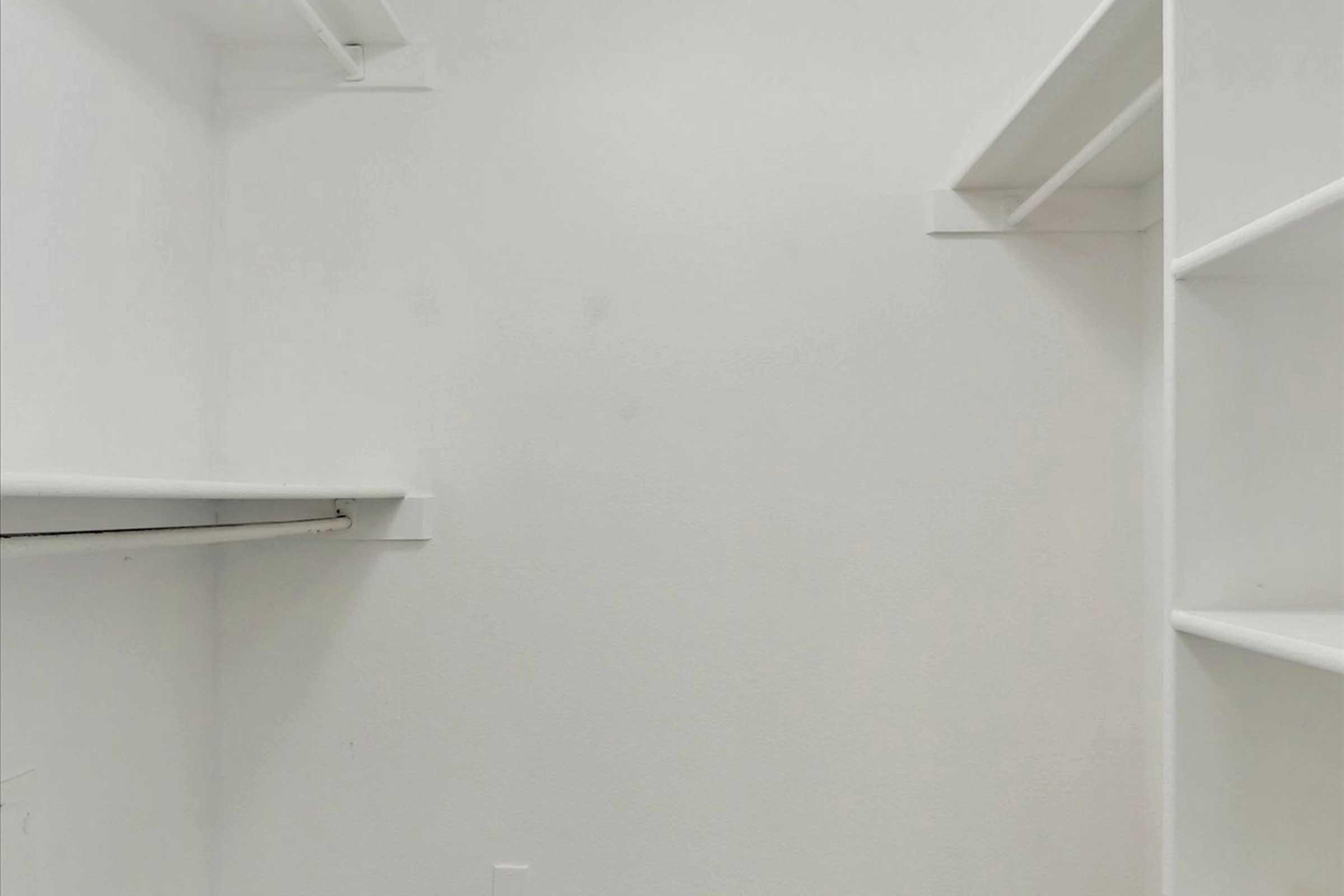 Empty walk-in closet with white walls and multiple shelves. The space is well-lit but lacks any visible items or decorations.