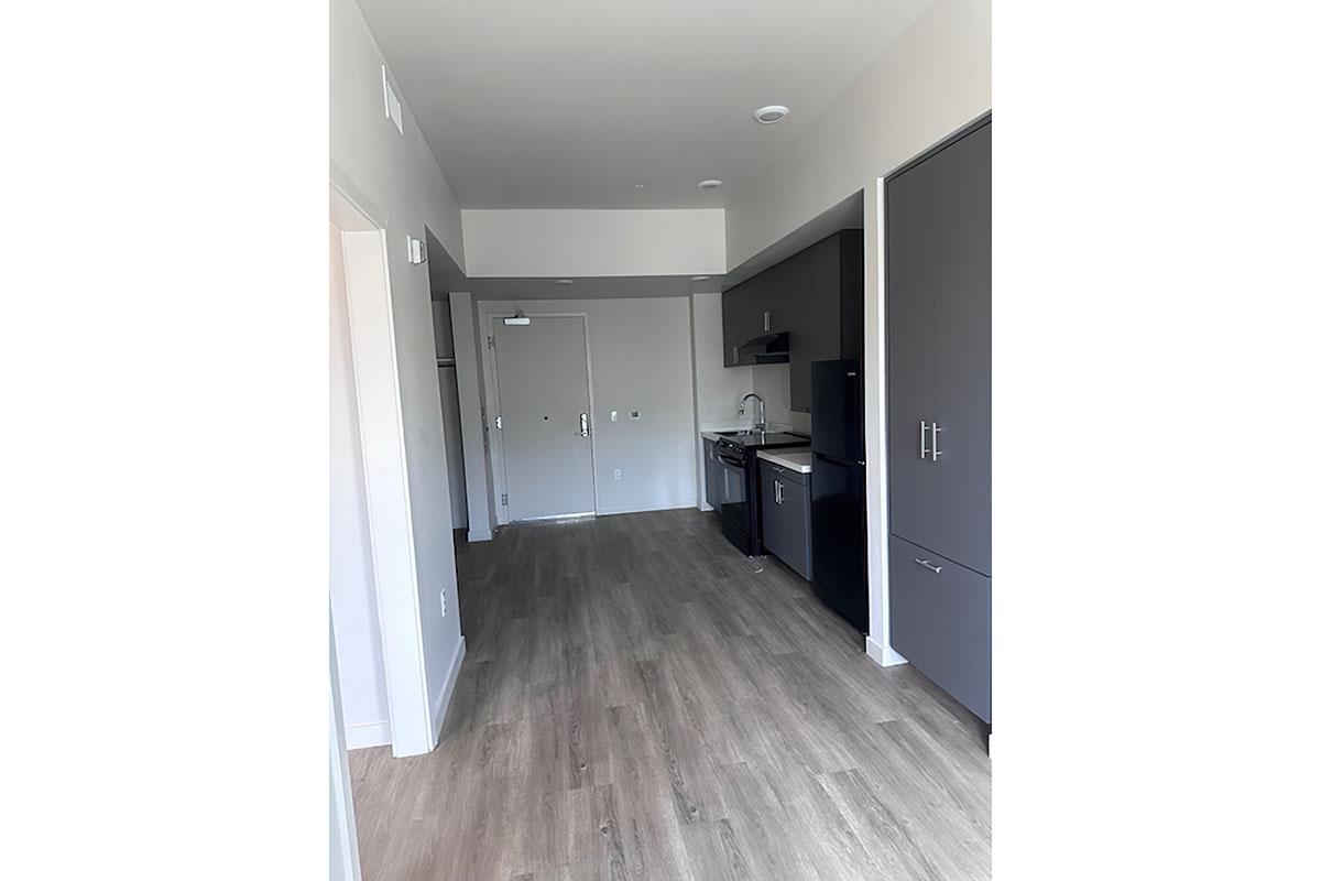 A modern apartment interior featuring a kitchen with dark cabinetry and black appliances.