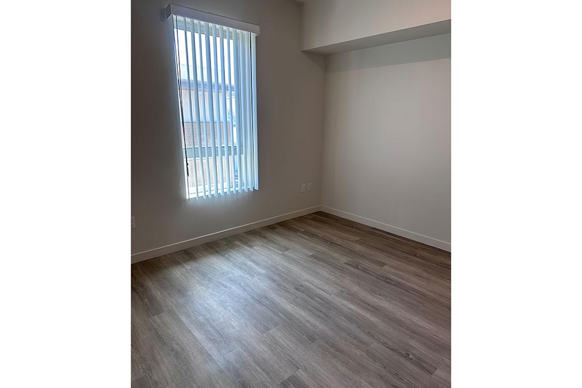 Empty interior of a room with light-colored walls and wooden flooring.