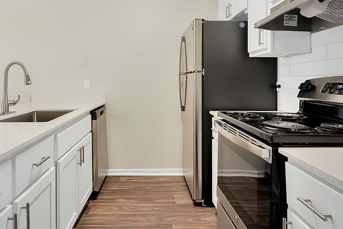 Modern kitchen featuring white cabinets, stainless steel appliances including a refrigerator, dishwasher, and stove. The countertop is a light color with a sleek design. The flooring is wood laminate, providing a warm and inviting atmosphere. The walls are painted a neutral shade.