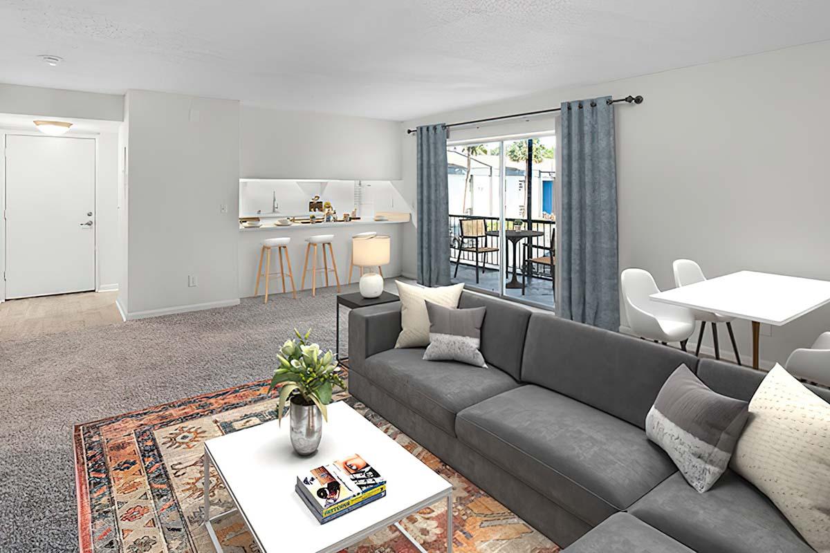 A modern living room featuring a gray sectional sofa with decorative pillows, a white coffee table with a vase of flowers, and a rug. There’s a dining area with white chairs and a table, and large sliding doors leading to an outdoor patio. The walls are painted light and the decor is minimalistic and stylish.