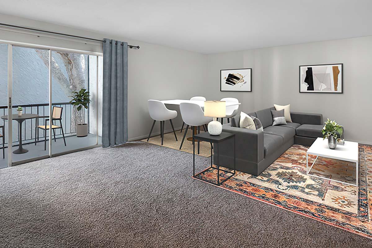A modern living room featuring a gray sofa with decorative pillows, a white coffee table, and a stylish area rug. There is a dining area with white chairs and a table, along with sliding glass doors leading to a small balcony. Natural light fills the space, creating a bright and inviting atmosphere.