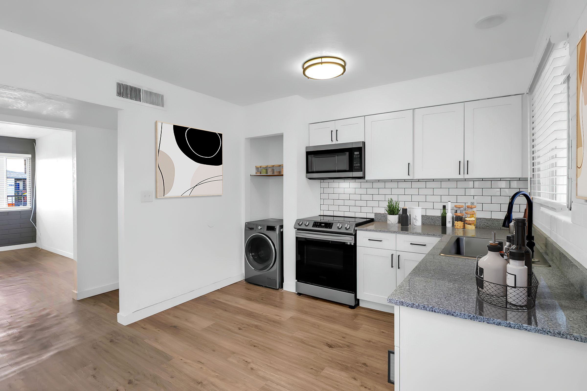 A modern kitchen featuring white cabinetry, stainless steel appliances, and a stylish backsplash. Includes a washing machine and an artistic wall decoration. The space has wood flooring and ample natural light, creating a bright and inviting atmosphere.