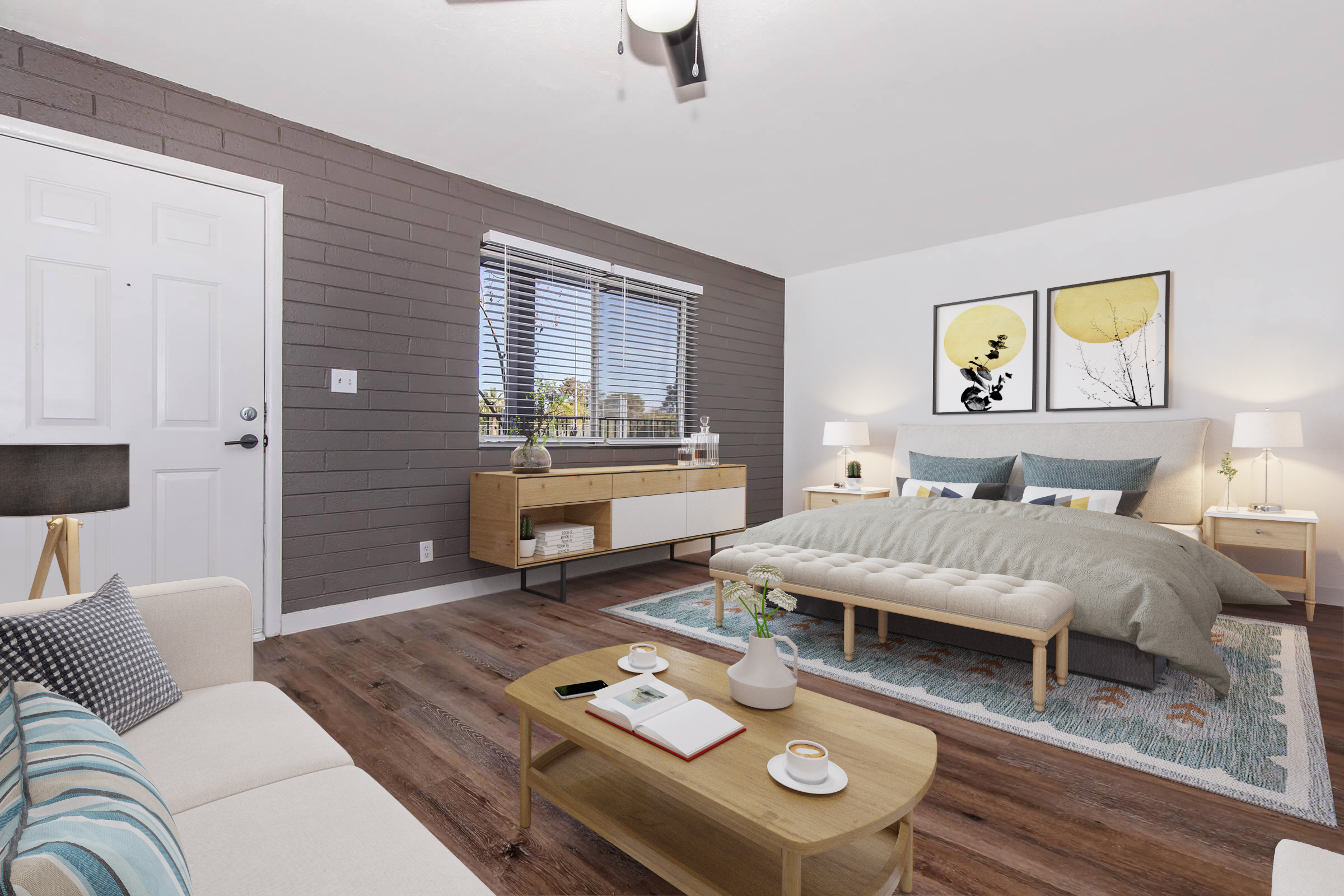 A cozy, modern bedroom featuring a comfortable bed with gray bedding, a stylish nightstand, and a wooden coffee table. The room includes a sofa, decorative pillows, and artwork on the walls. Natural light filters through the window, enhancing the welcoming atmosphere.
