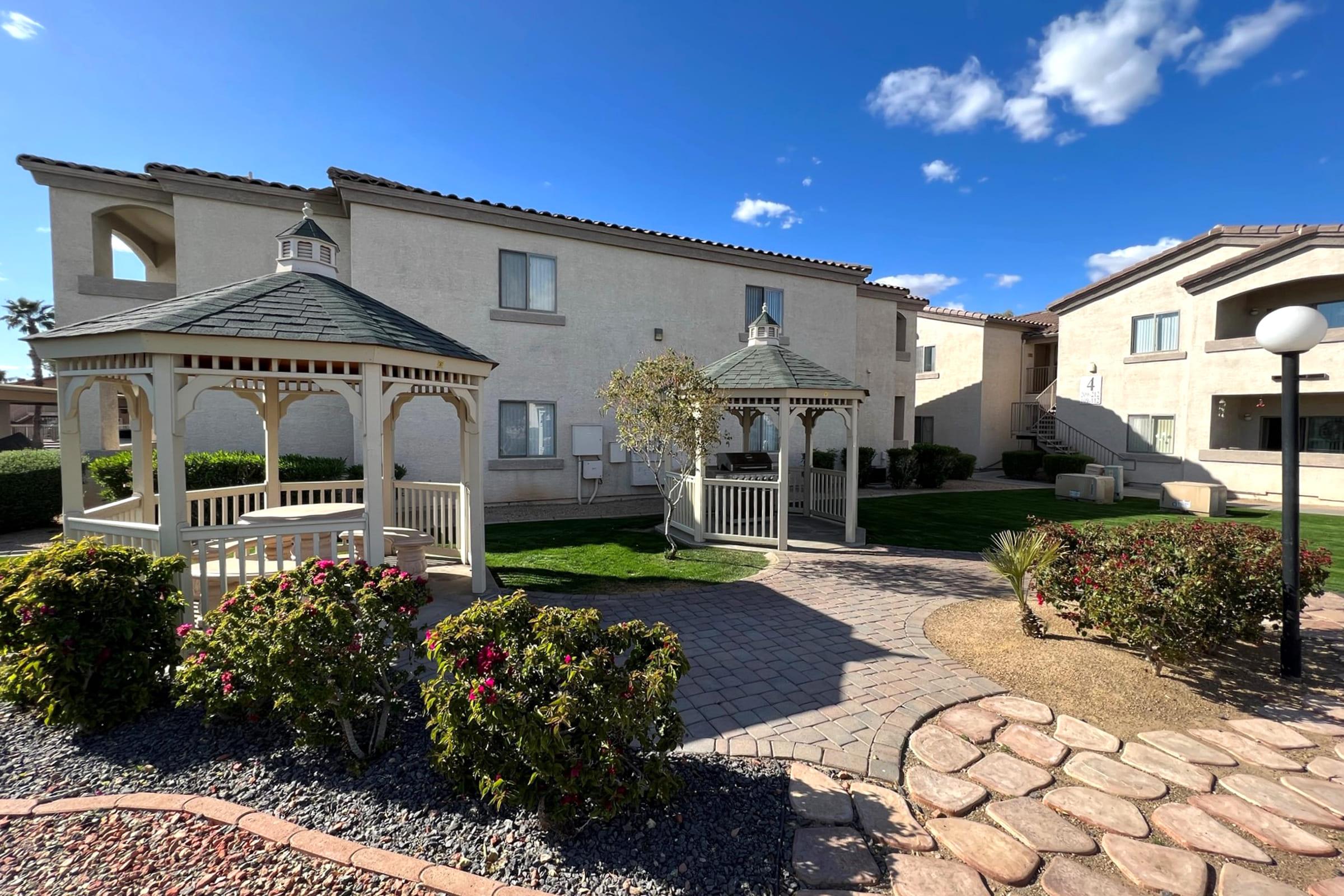 A landscaped courtyard featuring two white gazebos surrounded by vibrant flower bushes.