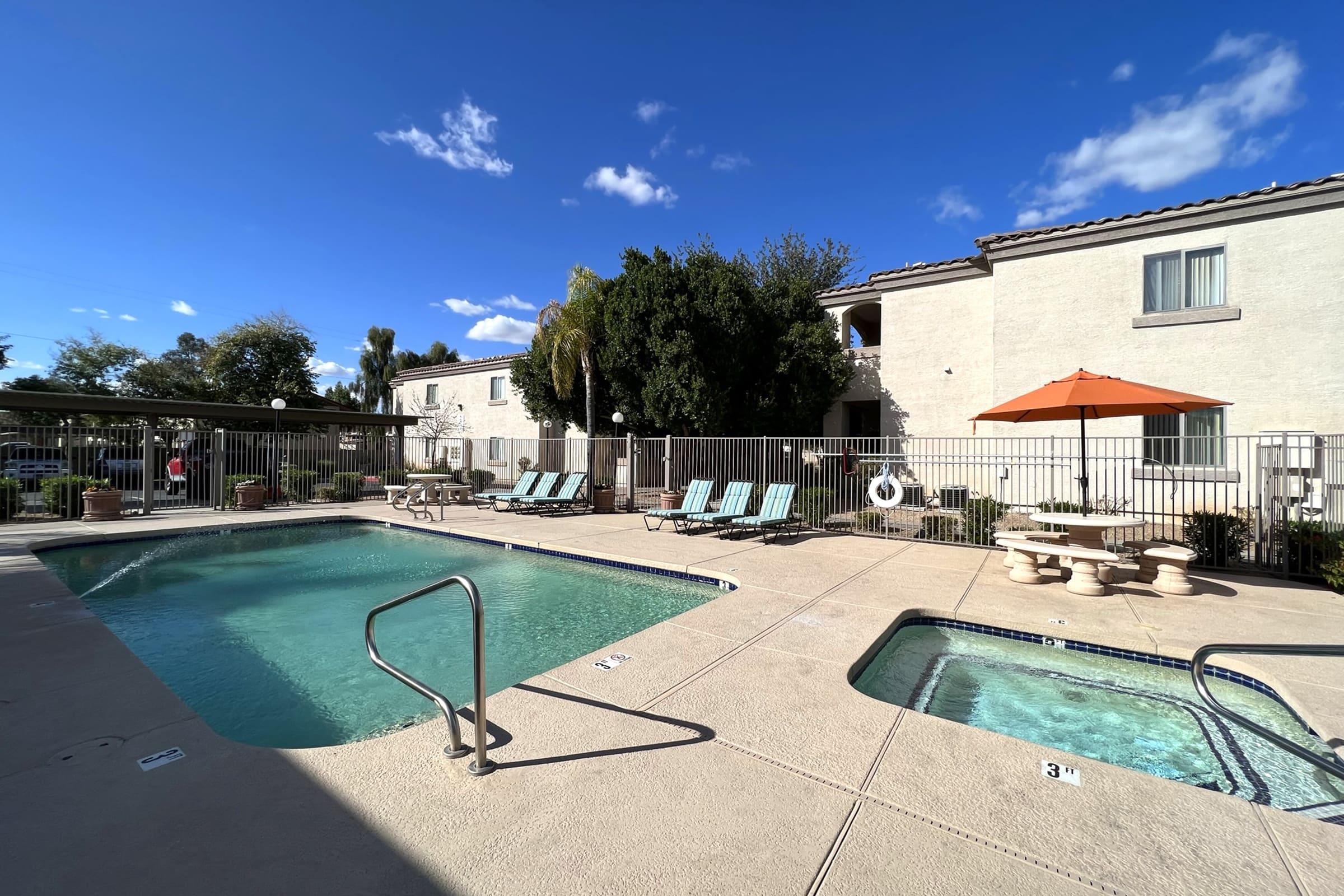A view of a pool area at a residential complex, featuring a large swimming pool and a hot tub.