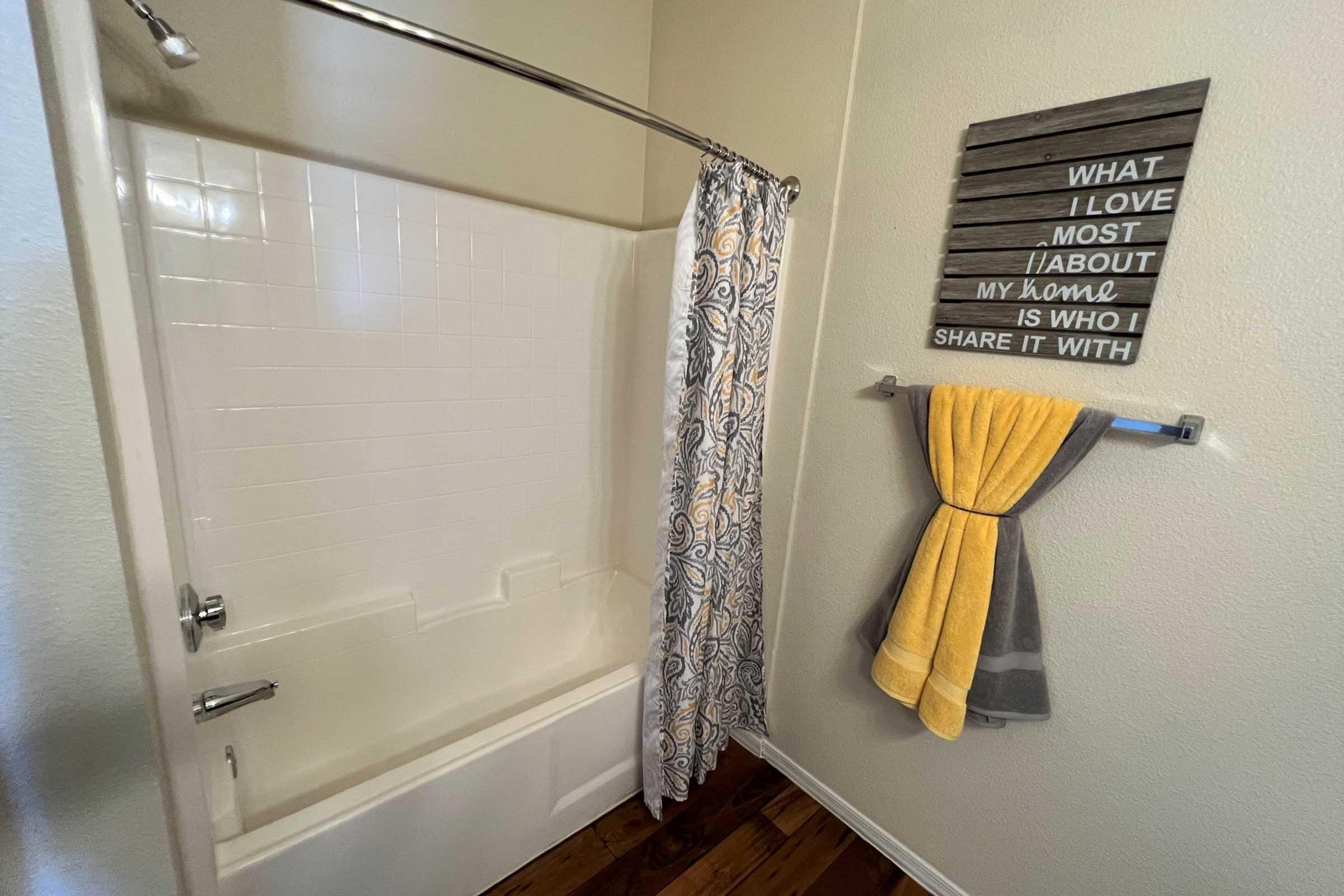 A clean bathroom featuring a bathtub with a shower curtain, a towel rack with a yellow and gray towel