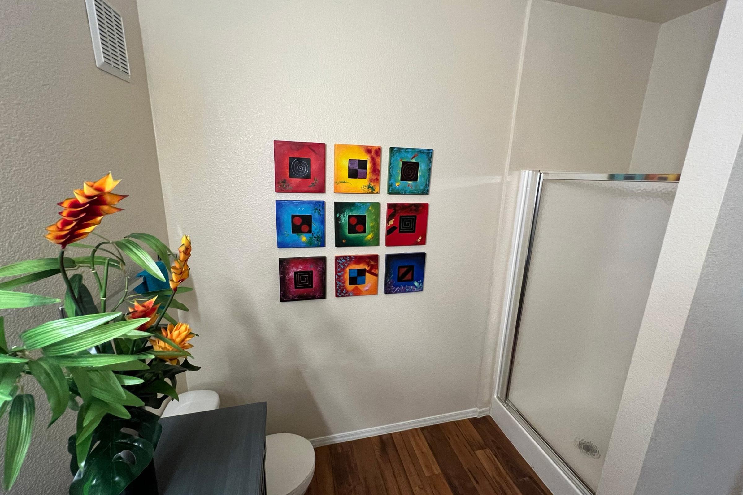 A corner of a bathroom featuring a colorful wall with eight geometric paintings arranged in two vertical columns.