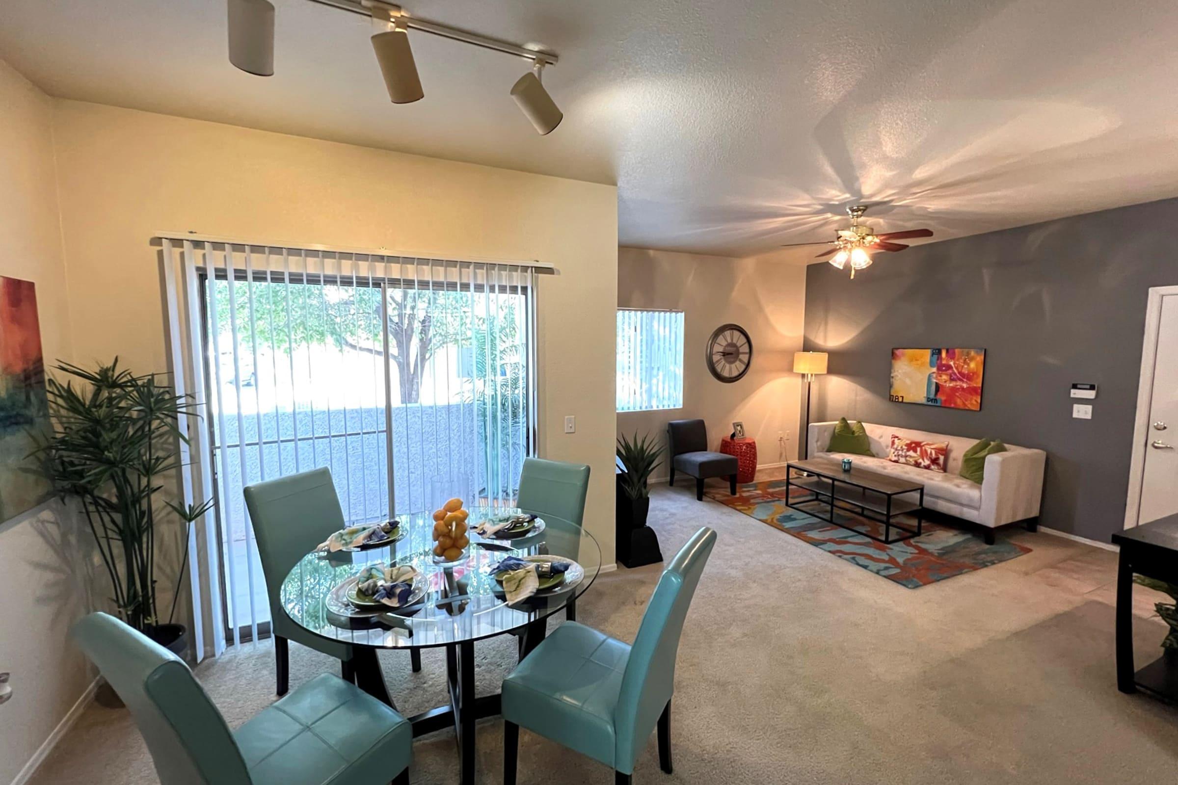 A well-lit living space featuring a dining area with a round table set for four, surrounded by turquoise chairs.