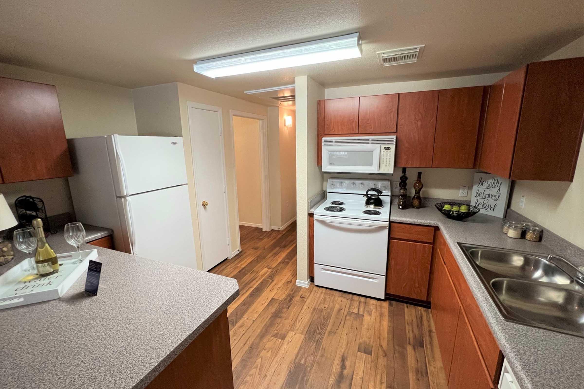 A modern kitchen featuring wooden cabinets, a double sink, a white stove and microwave, a refrigerator, and a neutral-colored wall. 