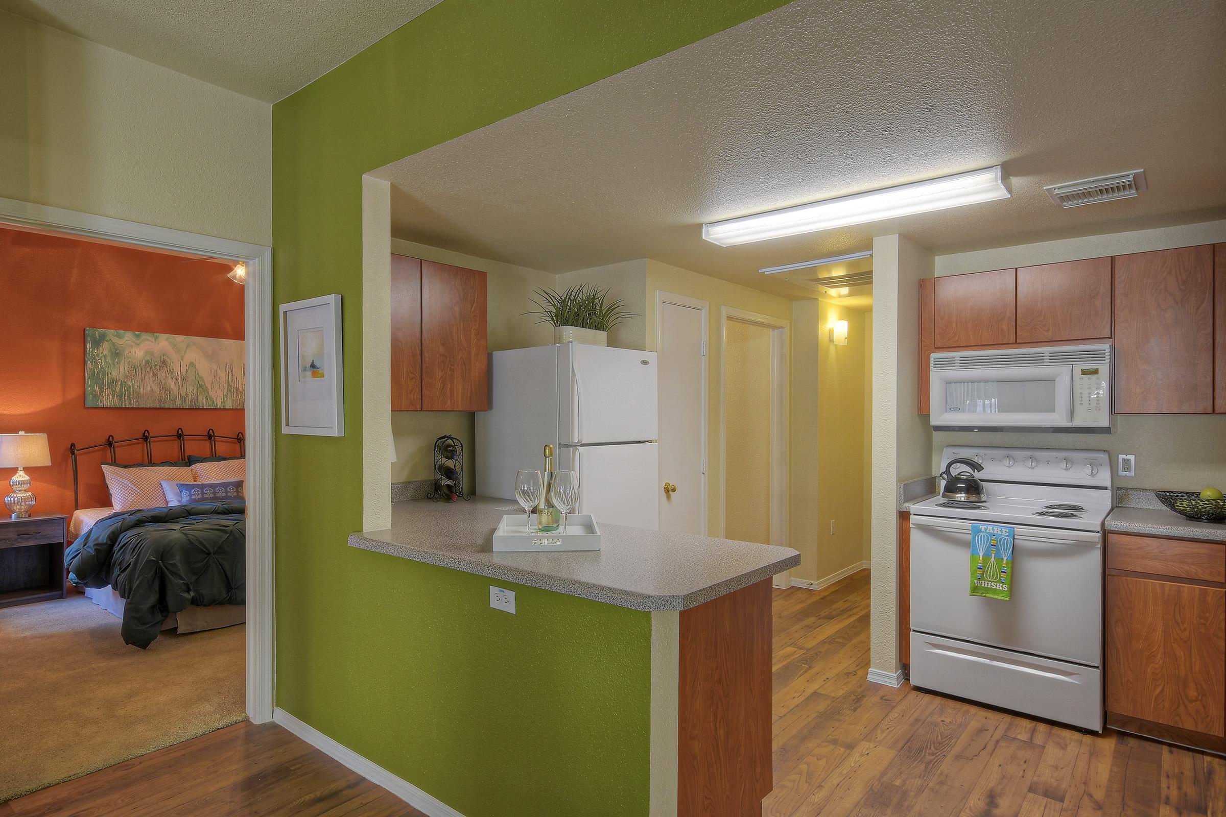A bright and modern kitchen with green accent walls, featuring wooden cabinets, a refrigerator, and a stove.