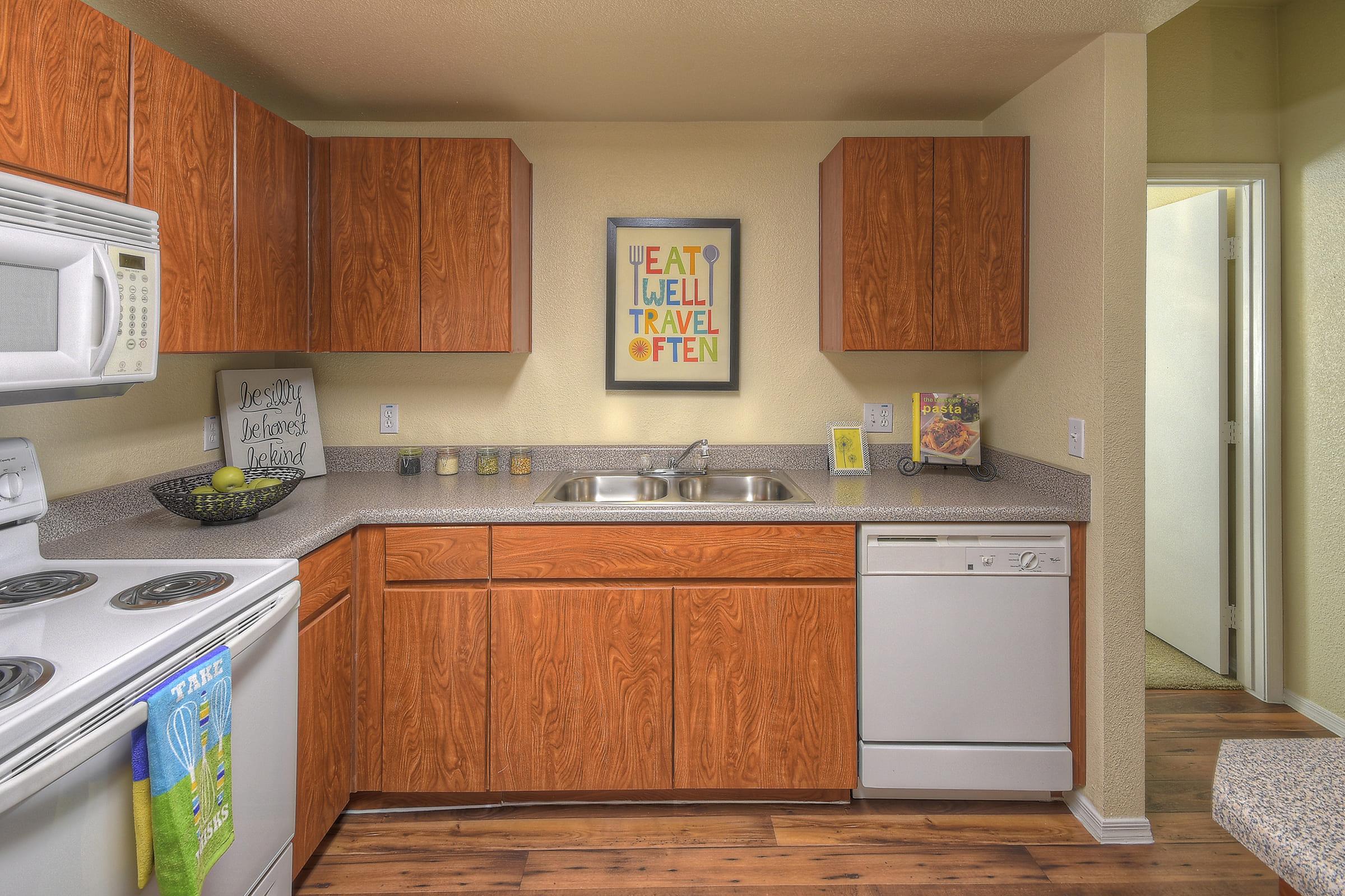A modern kitchen featuring wooden cabinets, a double sink, a dishwasher, and a stove.