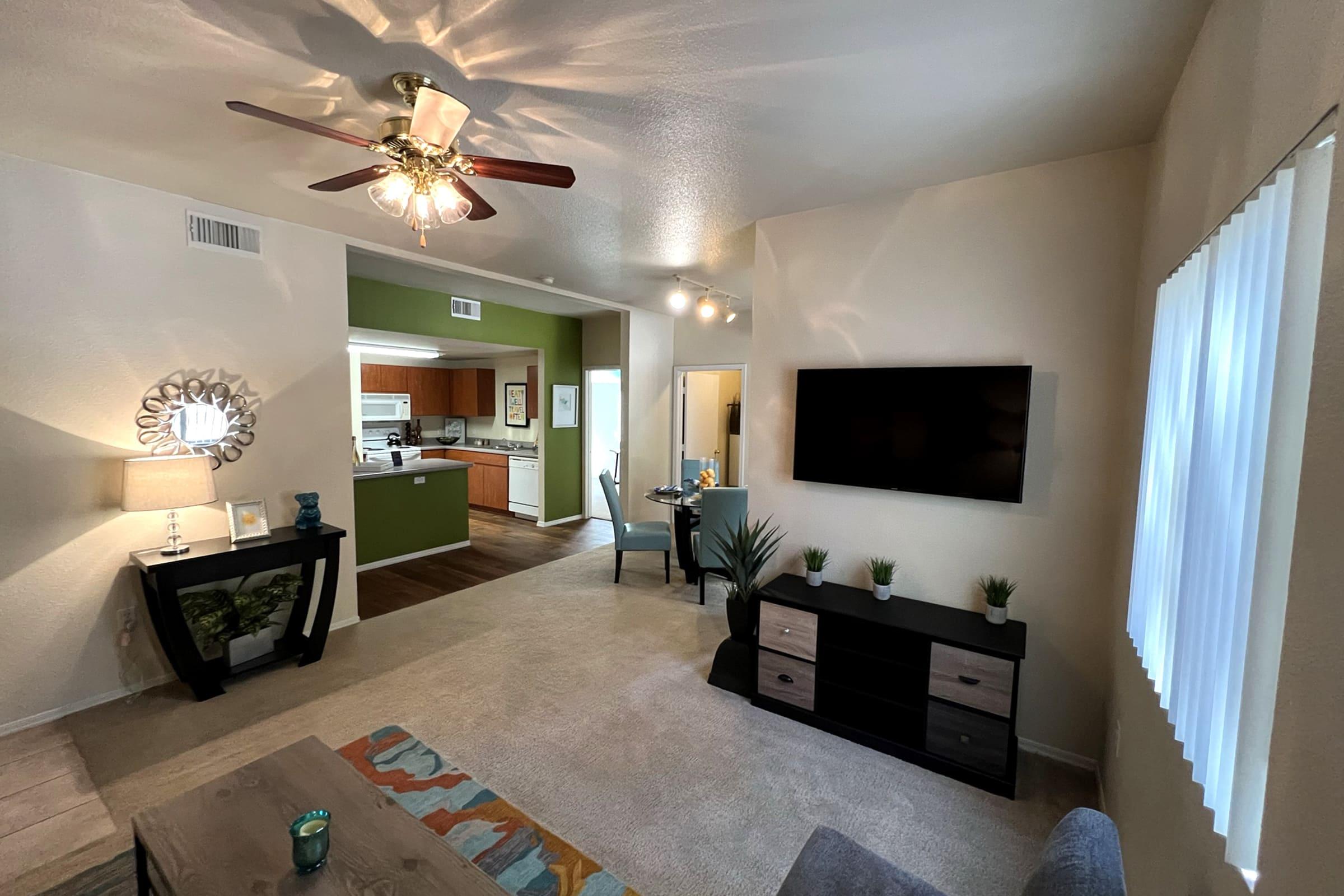 A cozy living room featuring a ceiling fan, a wall-mounted TV, and a coffee table with decorative items.