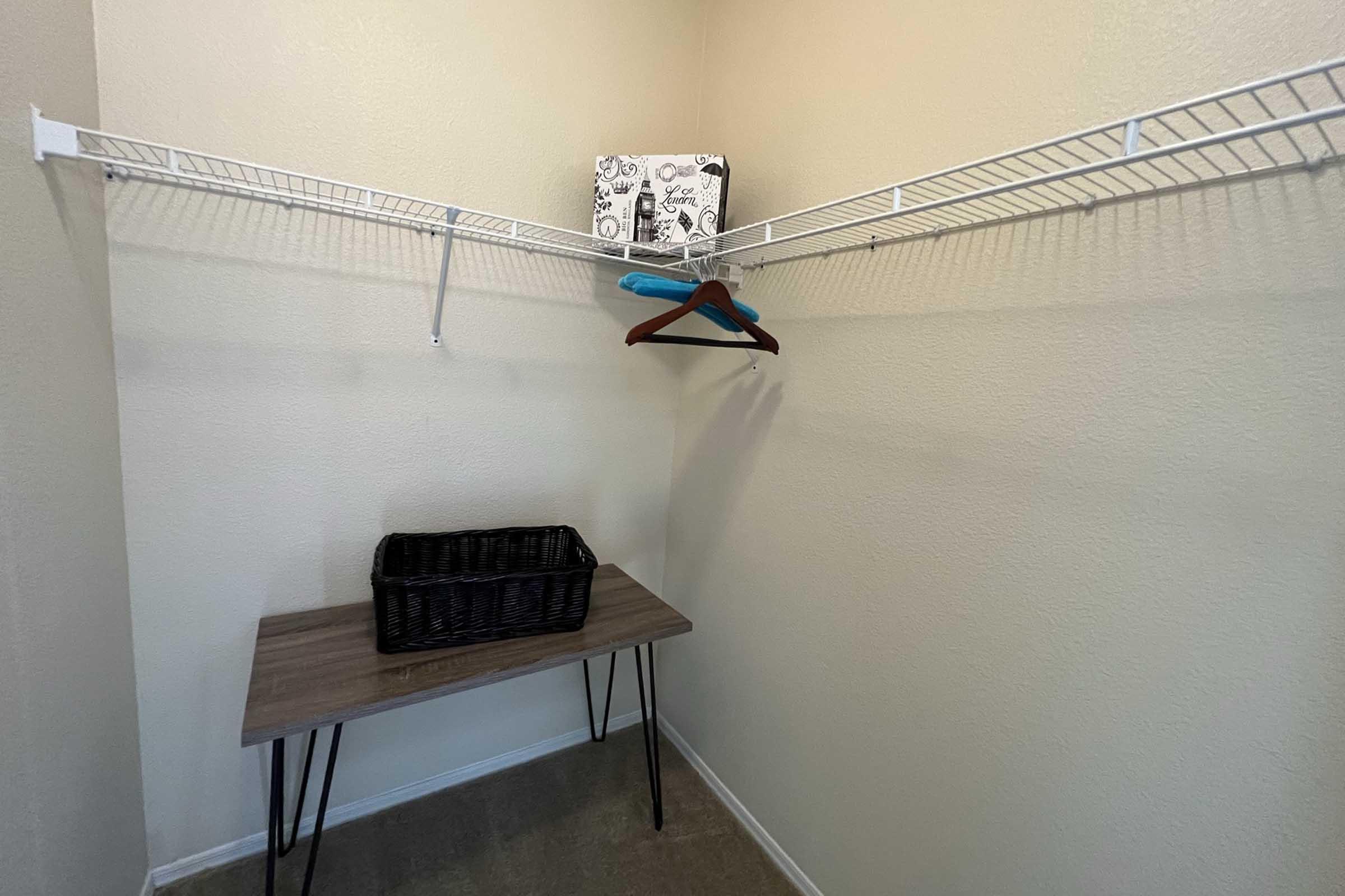 A small, empty closet with light-colored walls. There is a short shelf with a decorative box and a blue hanger hanging on it.