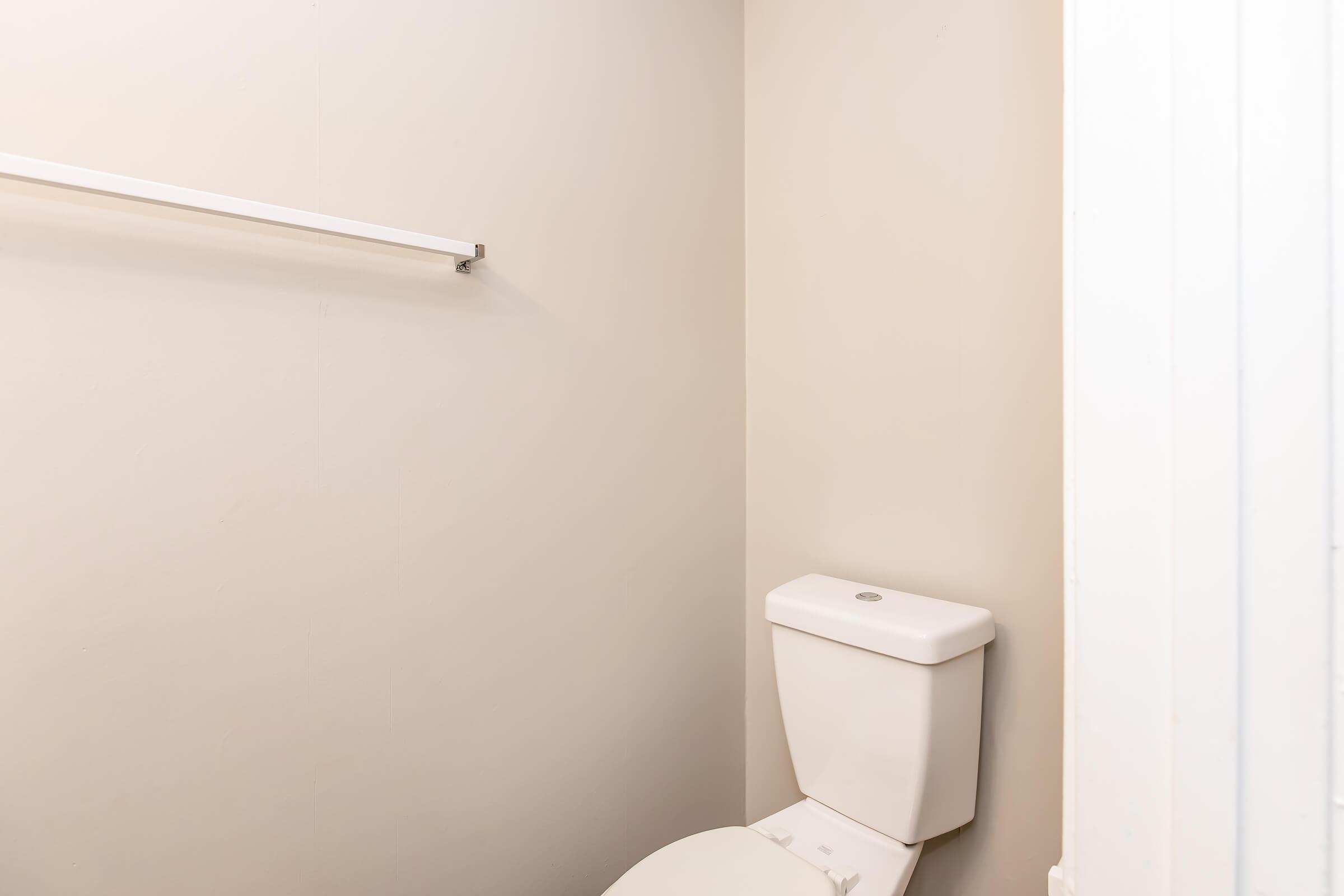 Interior view of a small bathroom featuring a white toilet and a towel rack mounted on a light-colored wall. The space is minimalistic and well-lit, with a simple and clean design.