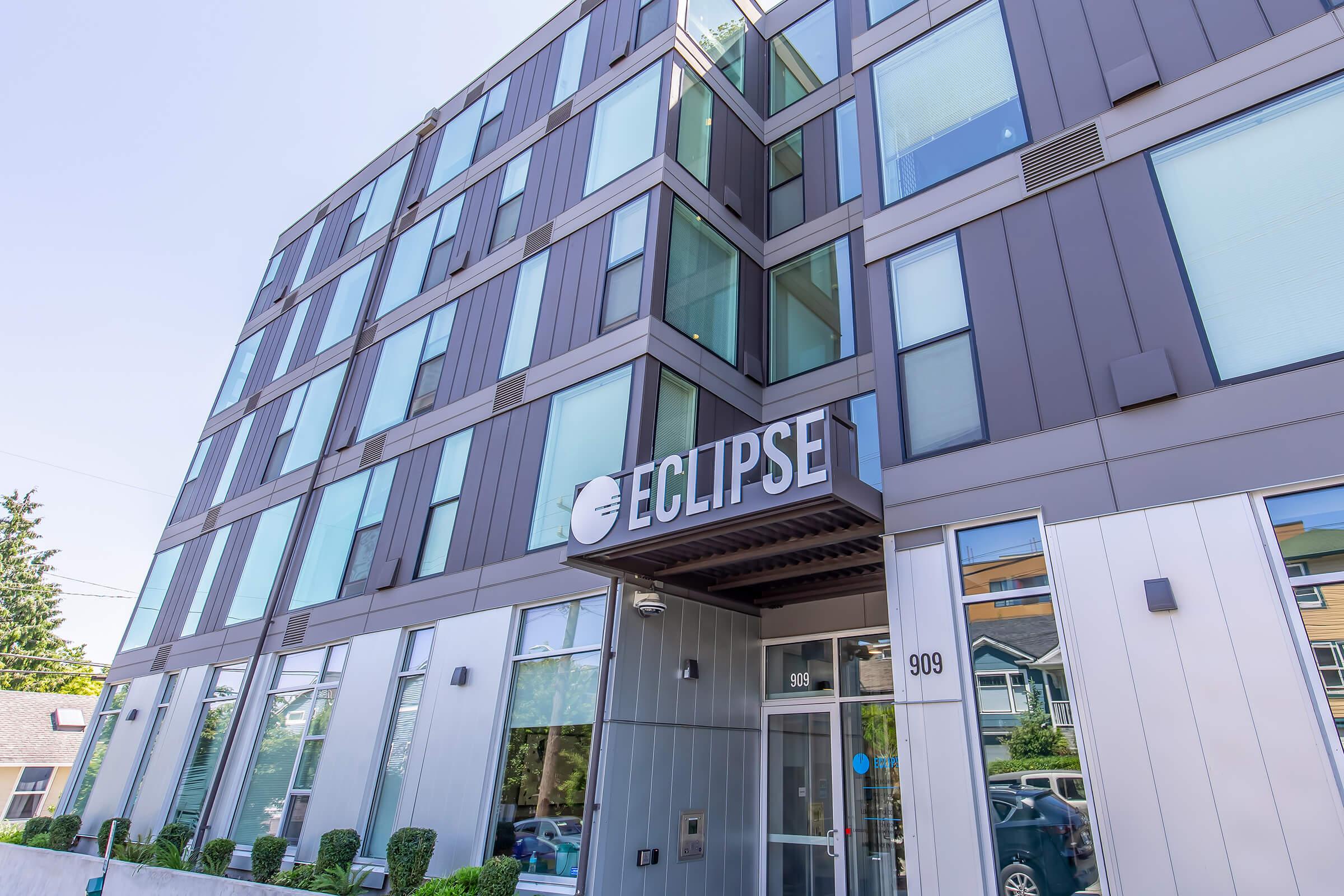Modern building with a sleek facade, featuring large windows and a prominent sign that reads "ECLIPSE." The entrance is framed by glass doors and neatly trimmed shrubs, contributing to a contemporary and inviting appearance. The address visible is 909.