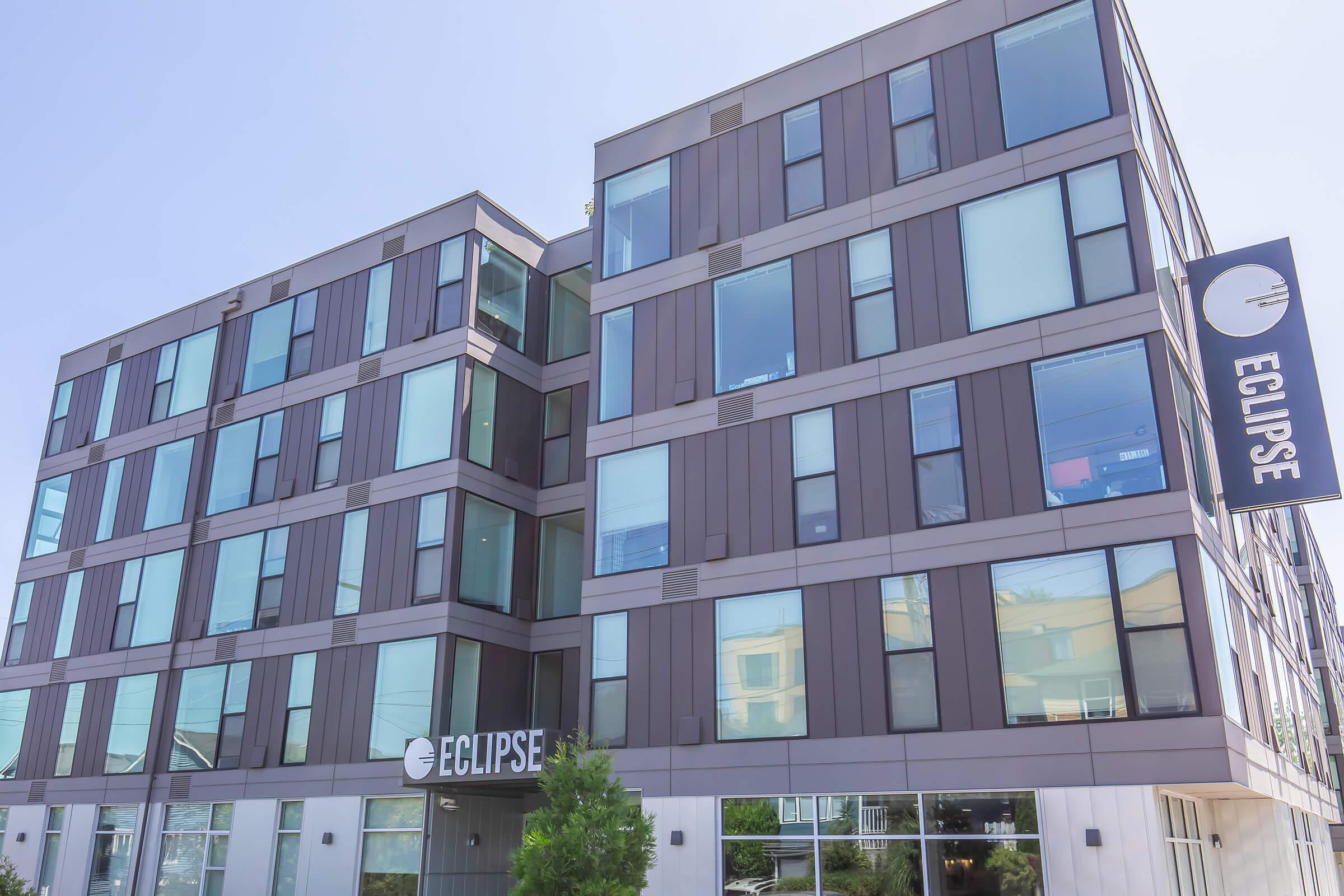 Modern building with a sleek, contemporary design featuring large windows and a sign that reads "ECLIPSE." The exterior is a combination of muted tones, giving it a stylish appearance. Surrounding the building is minimal landscaping, enhancing its urban aesthetic on a clear day.