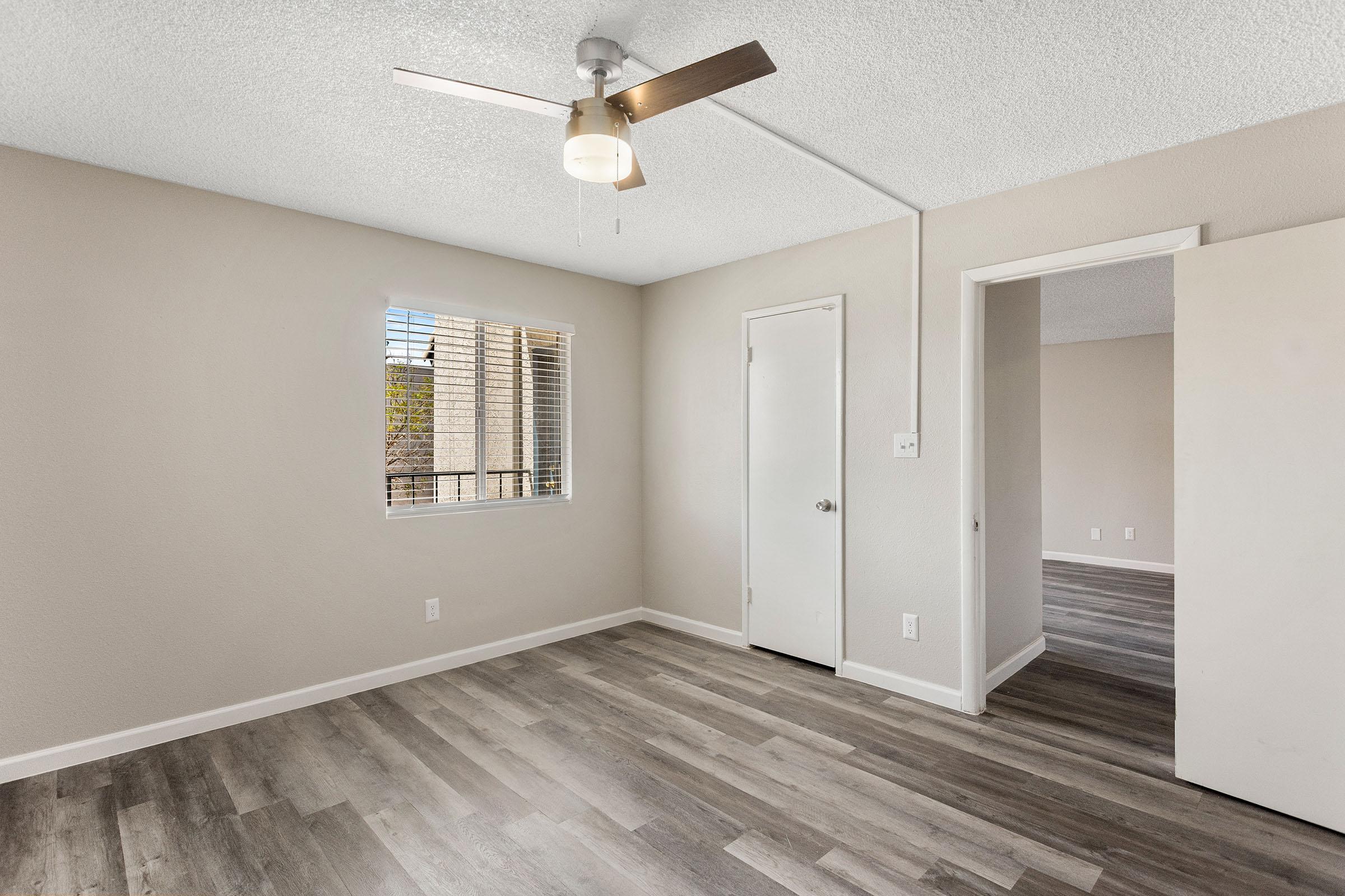 An apartment with a ceiling fan, wood-style flooring, and a window at Rise Thunderbird.