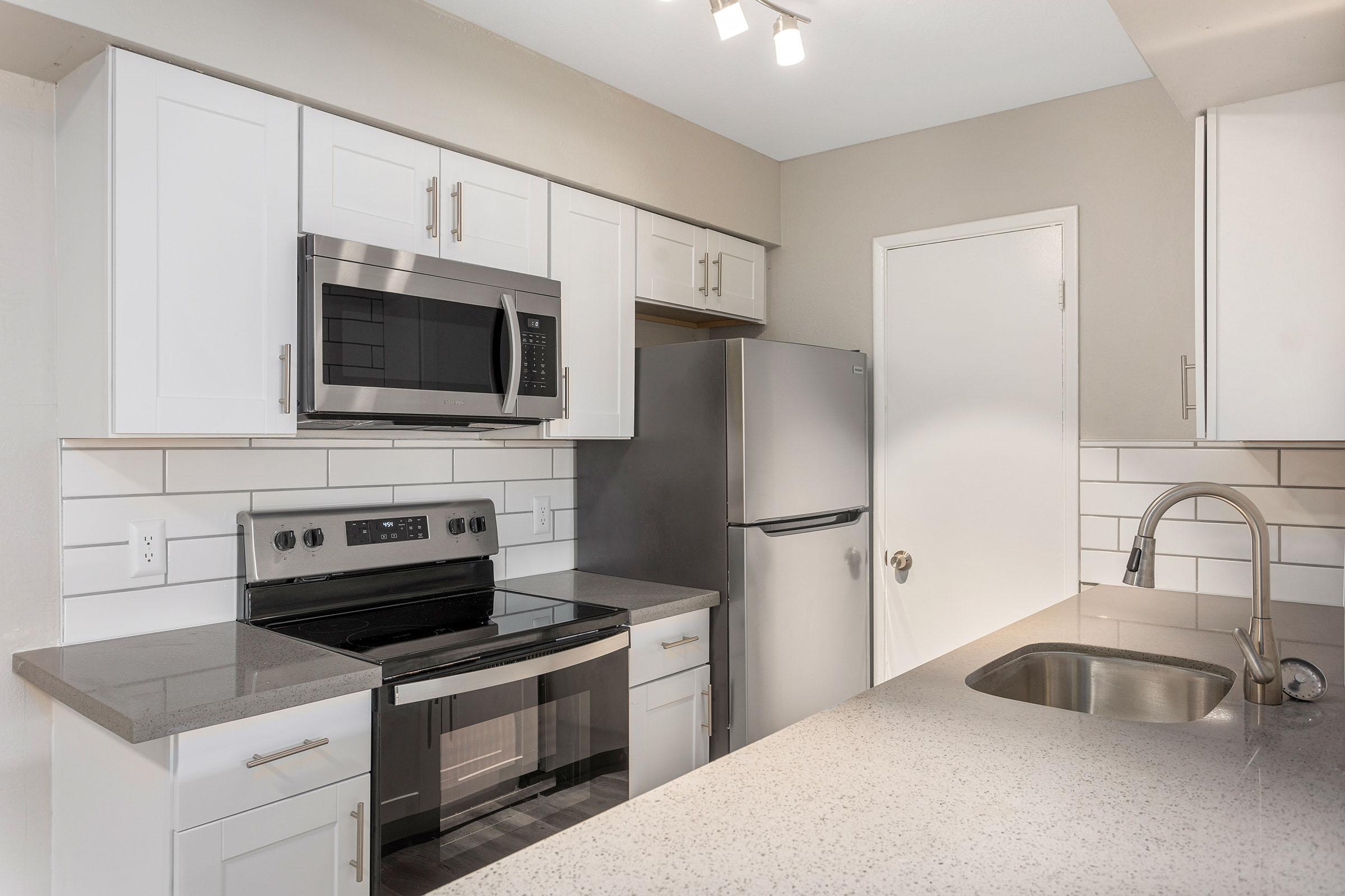 A kitchen with white shaker cabinets and grey countertops at Rise Thunderbird. 