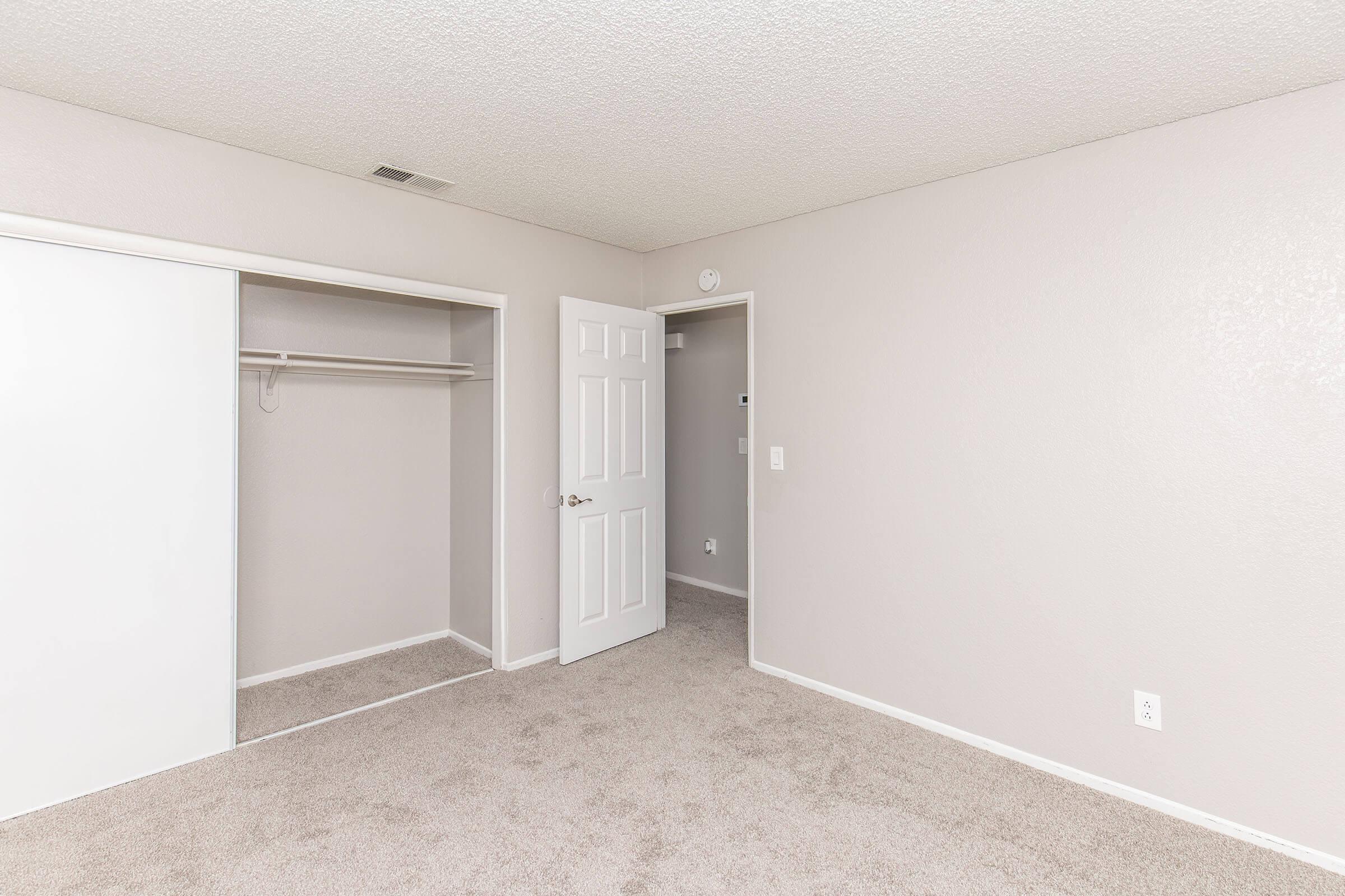 A vacant room featuring light beige walls and plush carpet. There is a white sliding closet door on the left and a closed interior door on the right. The space is well-lit and minimalistic, suitable for various furniture arrangements.