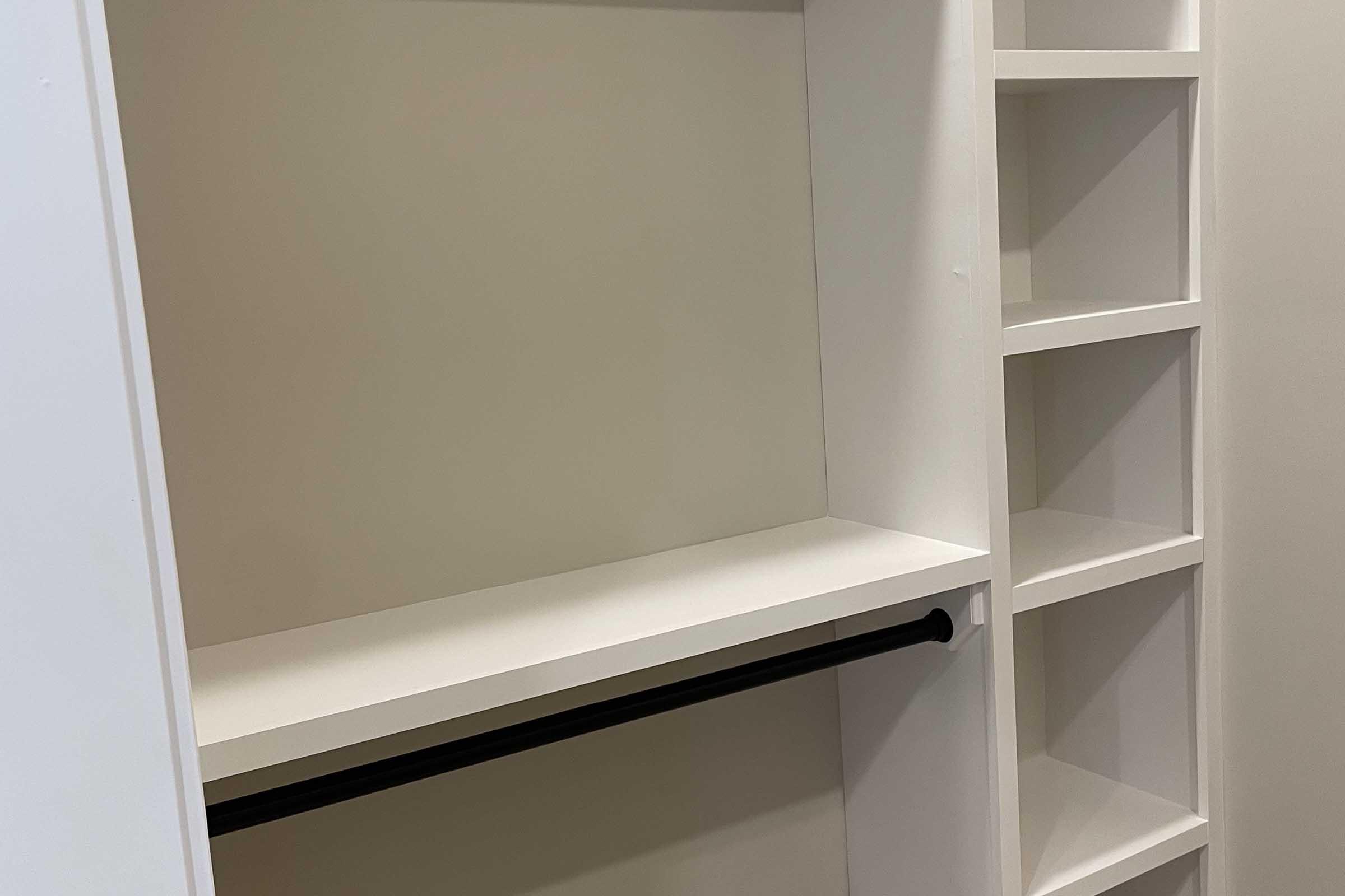 Empty closet space featuring a white interior, a black closet rod for hanging clothes, and built-in shelves on the right side for storage. The overall design is minimal and modern.