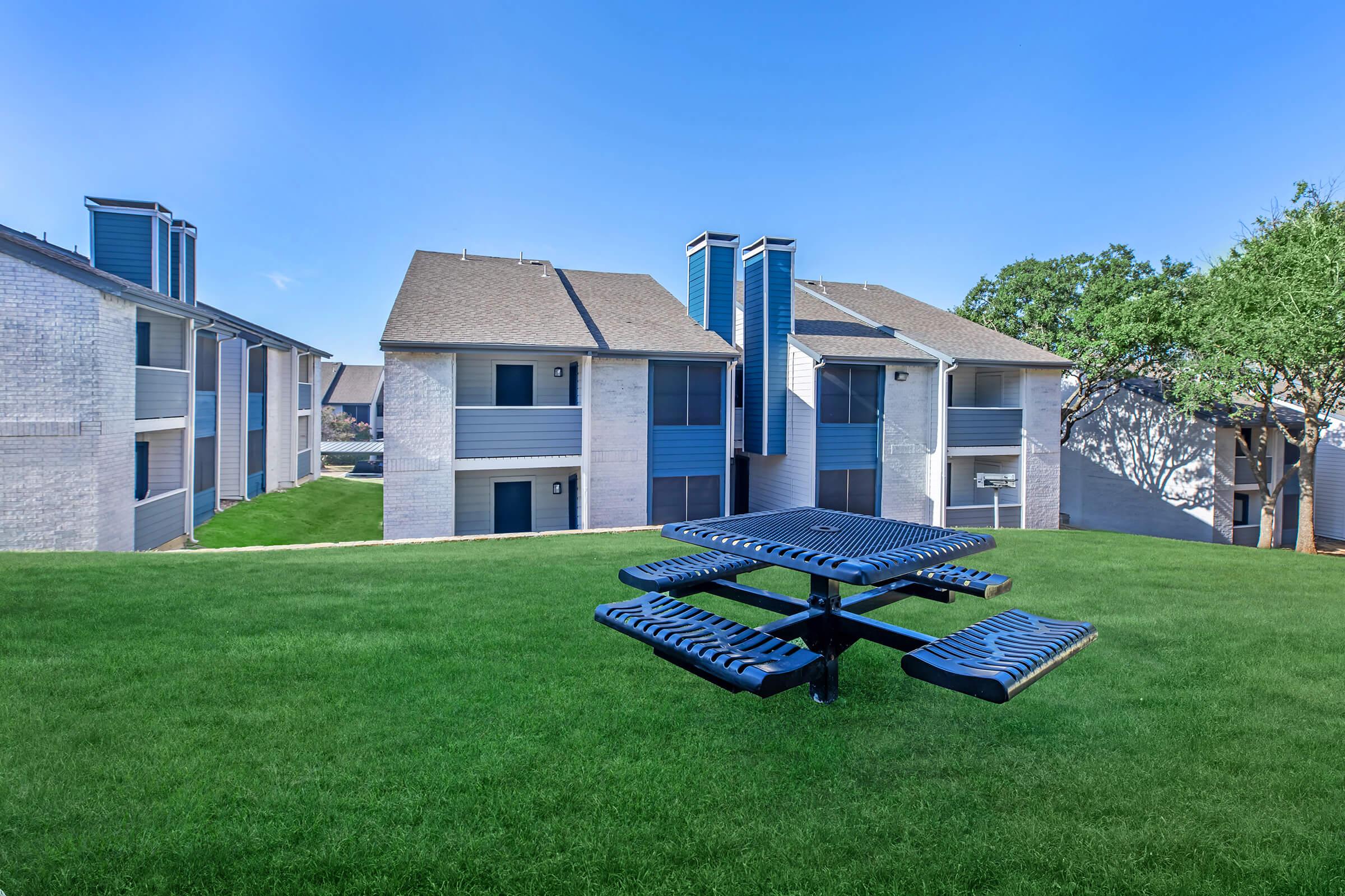Blue square table with four benches sitting on grass overlooking Bedford, TX apartments	