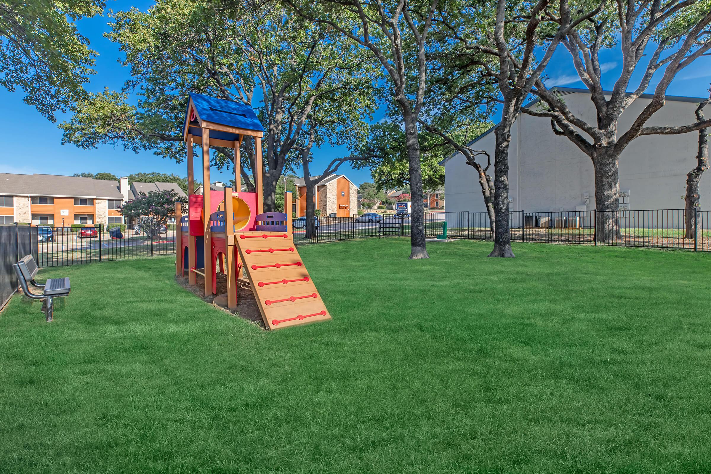 Outdoor grass-covered playground with trees and children's slide