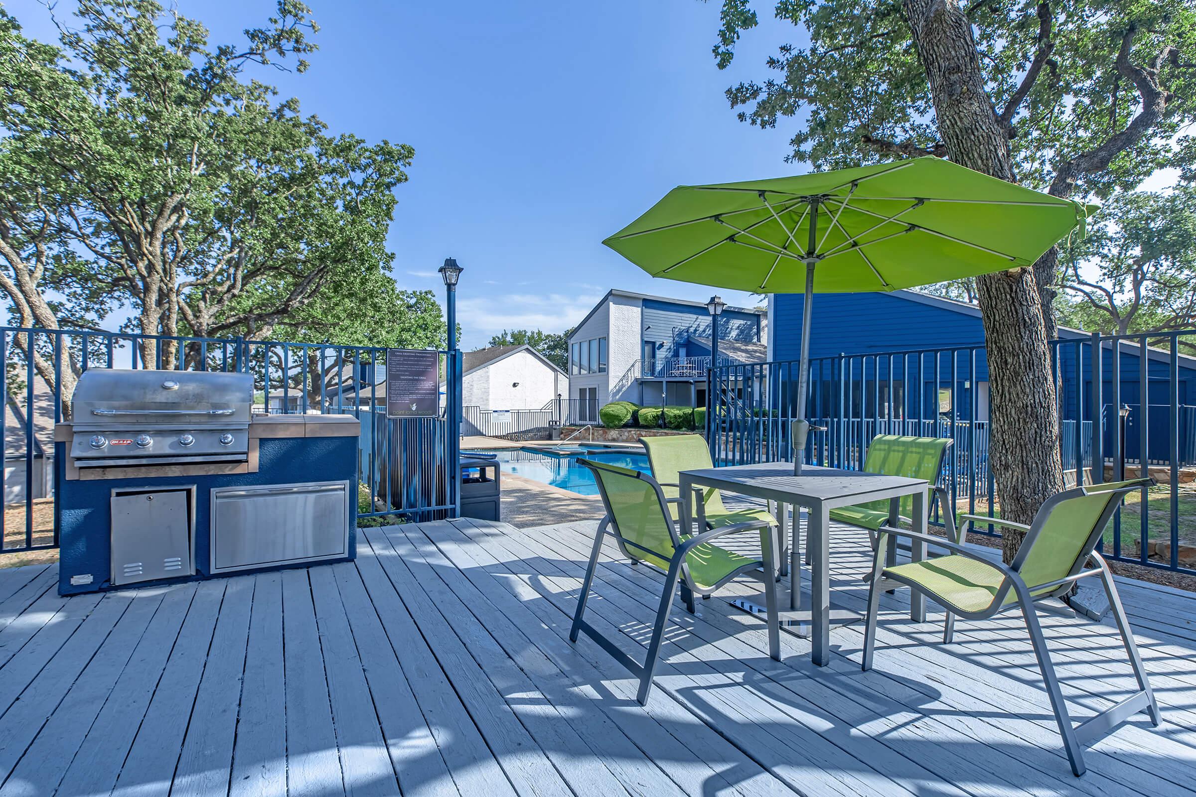 "Outdoor pool deck with a gas grill and lawn chairs and table under an umbrella