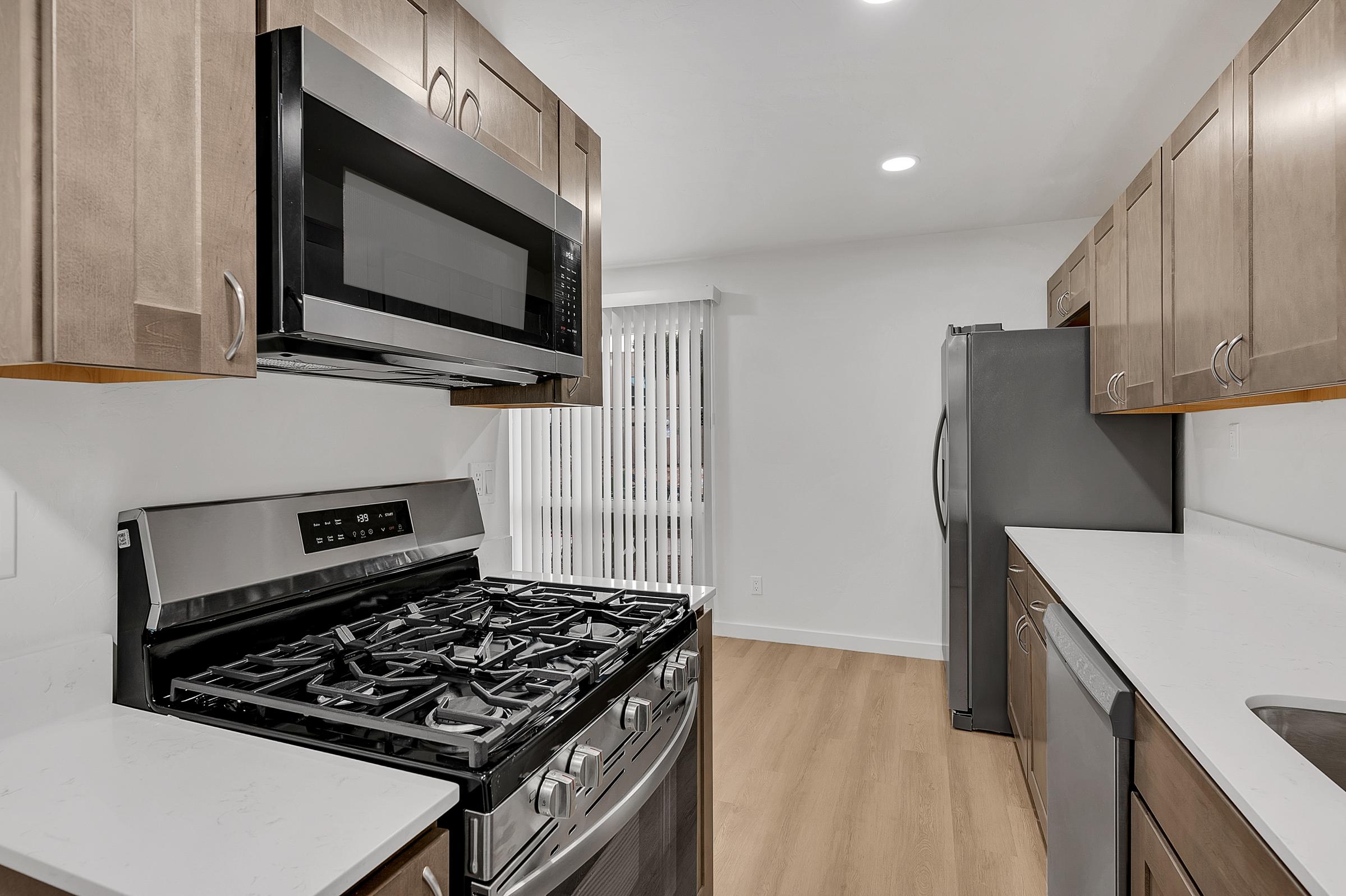 Modern kitchen featuring stainless steel appliances, including a gas range, microwave, and refrigerator. The cabinetry is a light wood finish, complemented by a white countertop and a spacious layout with natural light coming through the window. Elegant and functional design for cooking and entertaining.