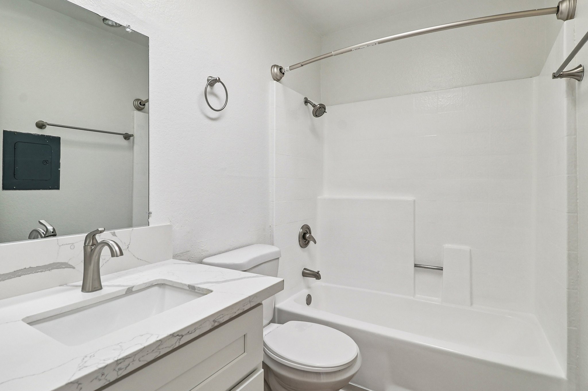 A modern bathroom featuring a white tiled bathtub with a shower, a sleek sink with a marble countertop, a mirror, and minimalistic fixtures. The walls are painted white, creating a bright and clean atmosphere.
