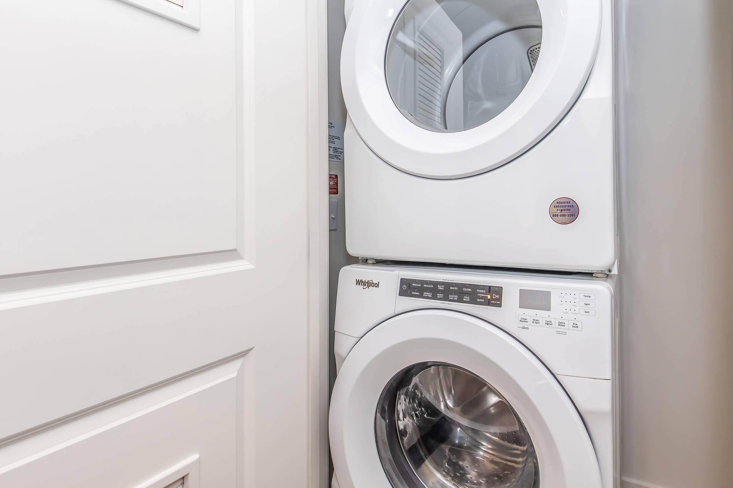 A stacked washer and dryer unit in a laundry space, featuring a white exterior. The door of the laundry area is partially visible on the left side, showcasing a compact and organized setup ideal for small spaces.