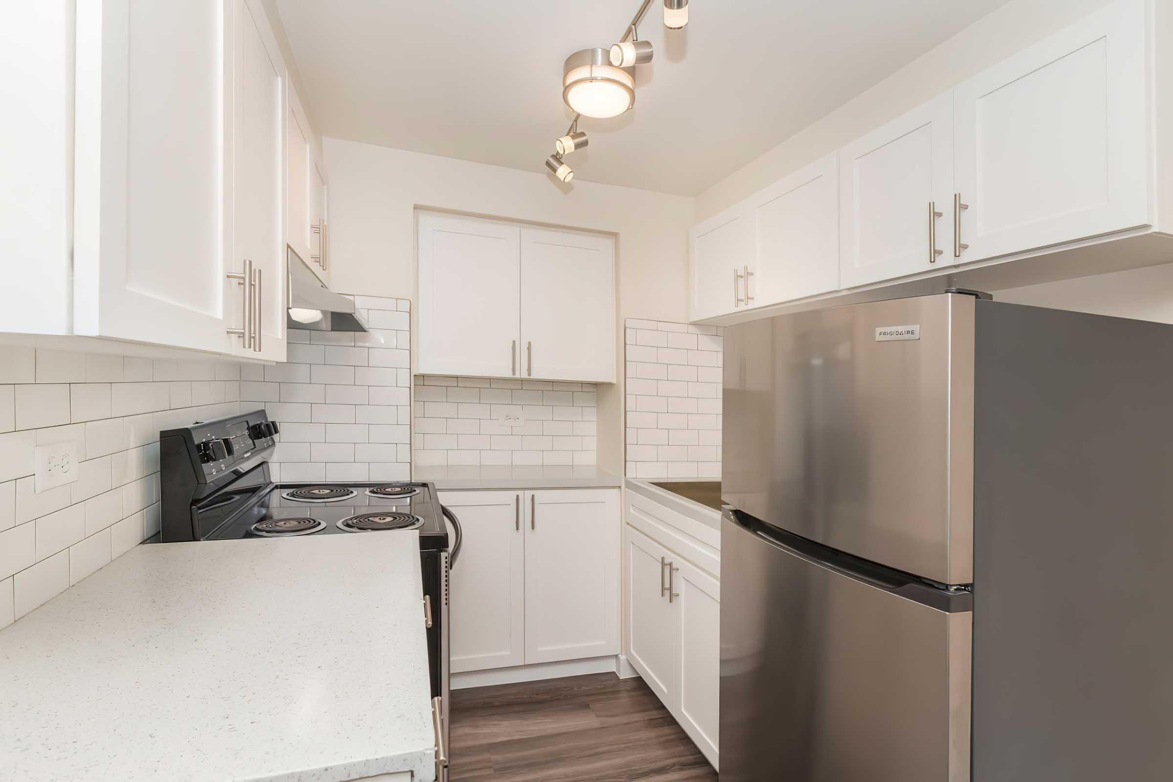 Modern kitchen featuring white cabinetry, a stainless steel refrigerator, a black stove with four burners, and a white countertop. 