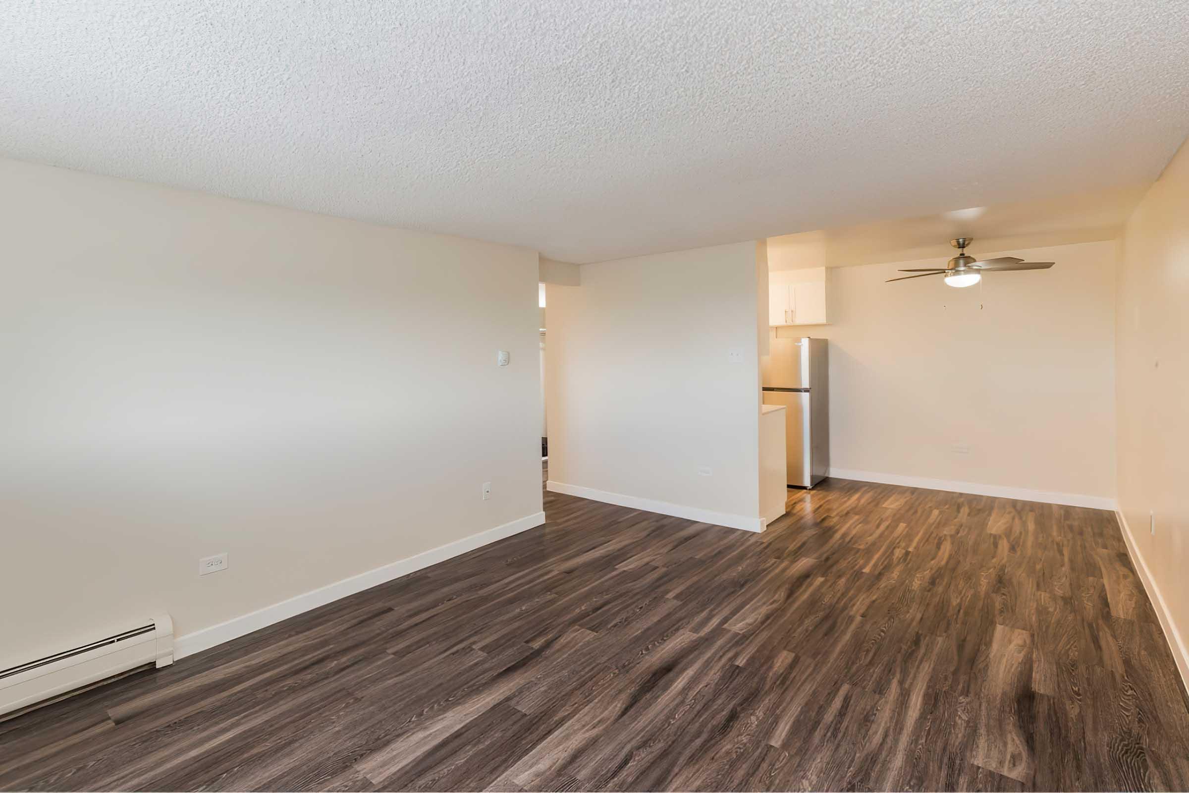 A spacious, empty living room with light-colored walls and modern wood-like flooring.