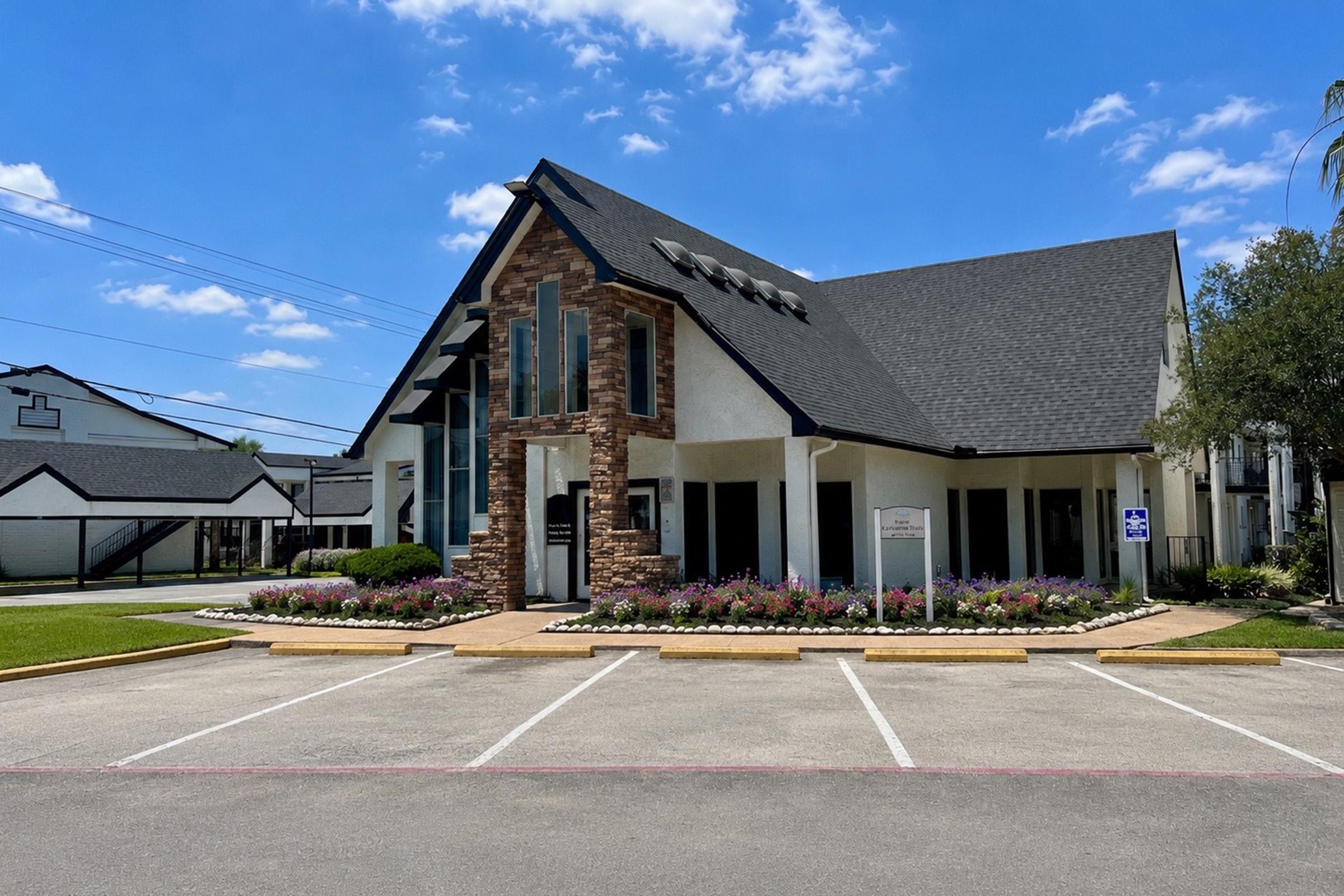 A well-maintained building with a modern architectural design featuring a stone accent and large windows. It is set in a landscaped area with a flower bed in front and several parking spaces. The sky is clear with a few clouds, indicating a sunny day.