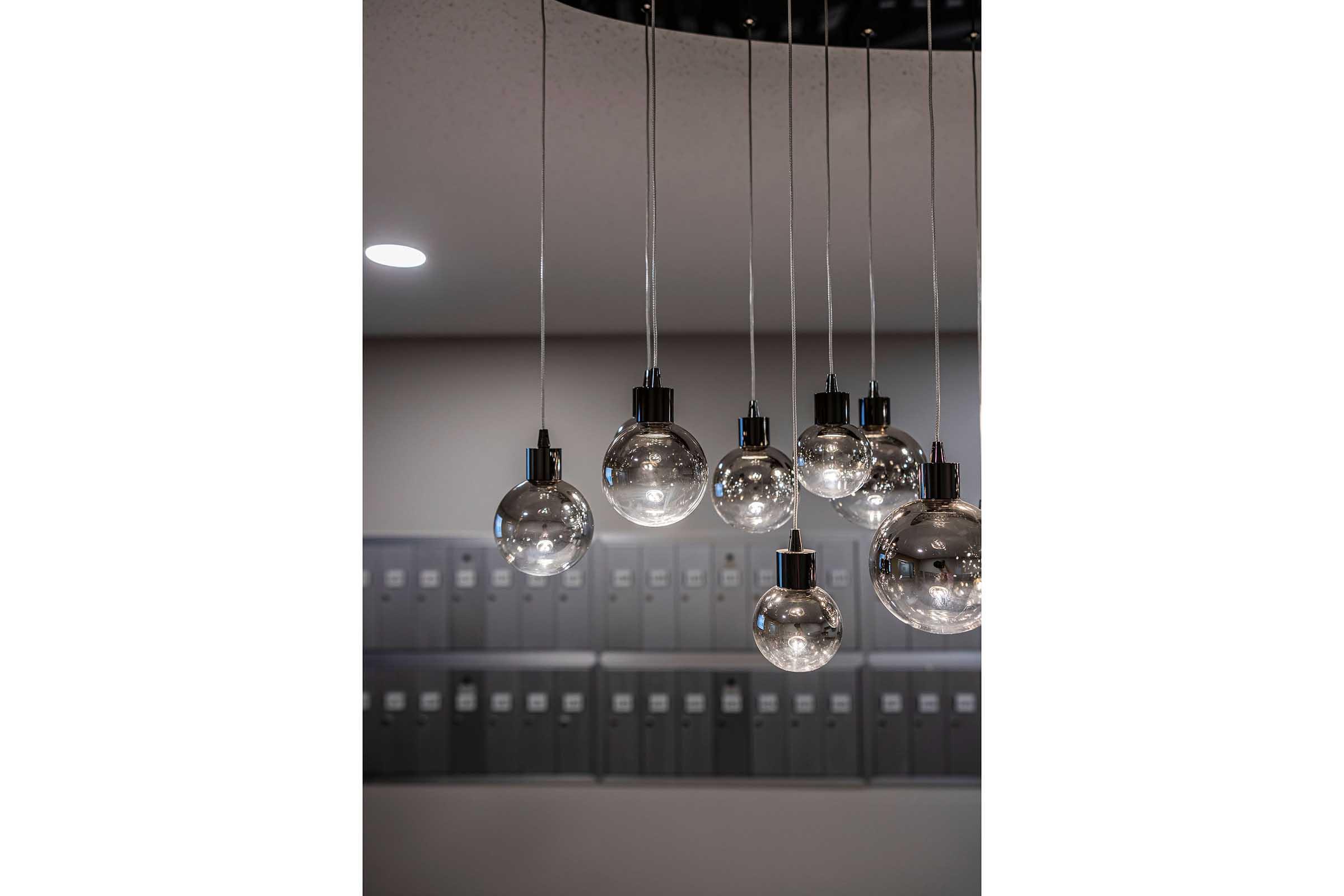 A close-up of modern pendant lights with clear glass bulbs, suspended from a minimalistic ceiling fixture. The background features neatly organized filing cabinets, enhancing the contemporary office or workspace ambiance.