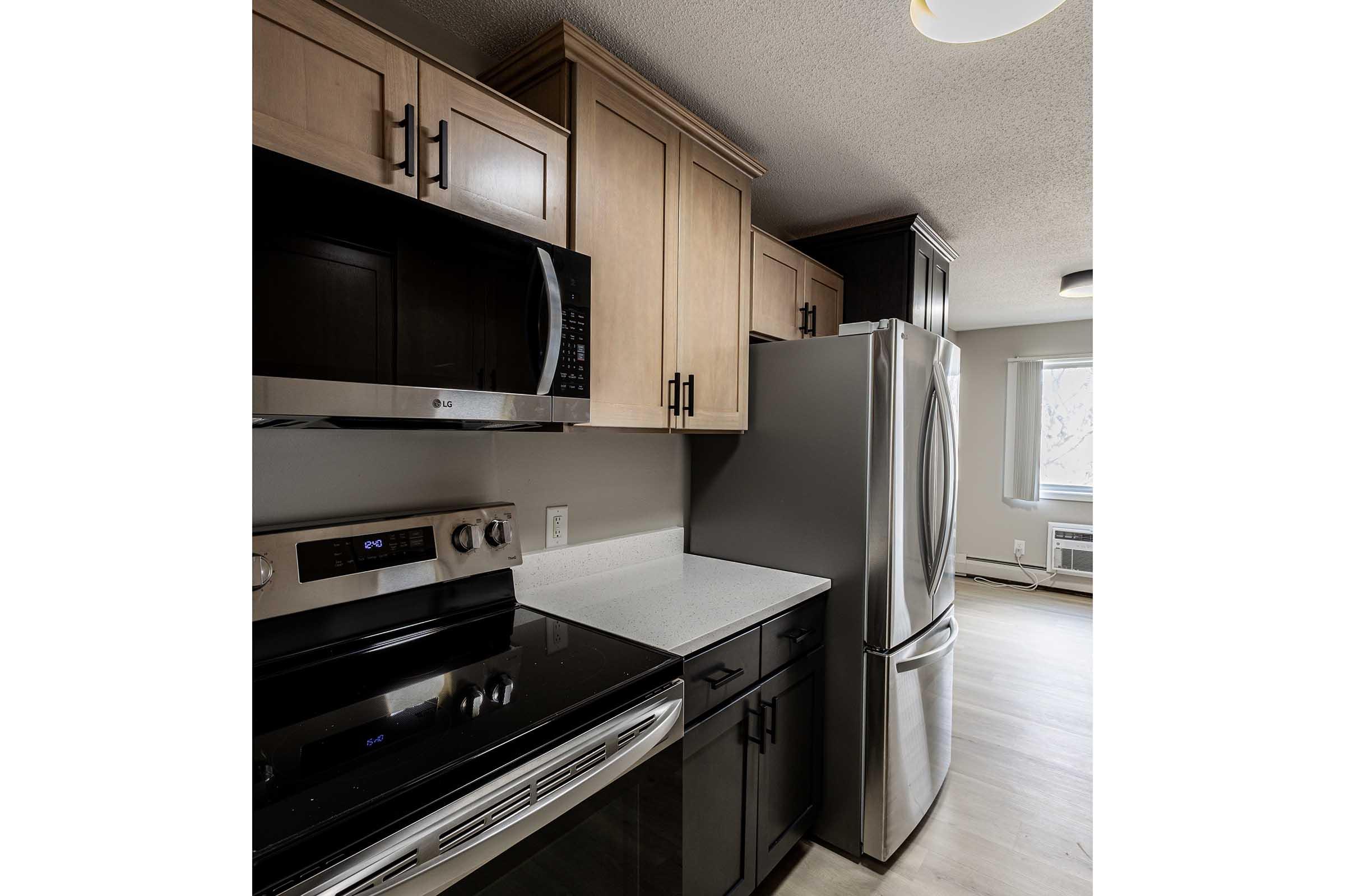 Modern kitchen featuring beige wooden cabinets, stainless steel appliances including a microwave, oven, and refrigerator, along with a white countertop. Natural light enters through a nearby window, creating a bright and inviting atmosphere.