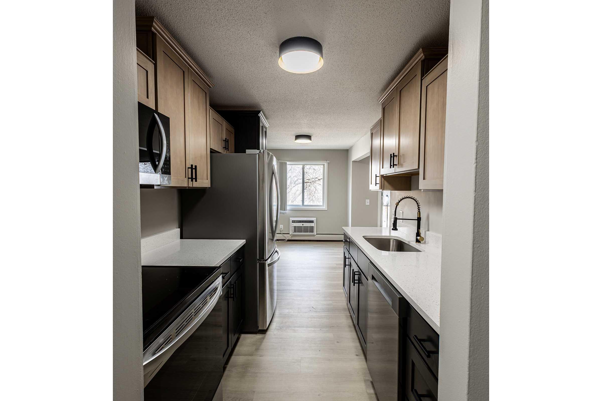 Modern kitchen featuring light-colored cabinets and dark countertops. Stainless steel appliances, including a refrigerator and microwave, are visible. A sleek sink with a faucet is installed on the counter. The space is well-lit with overhead lighting and has a window providing natural light.