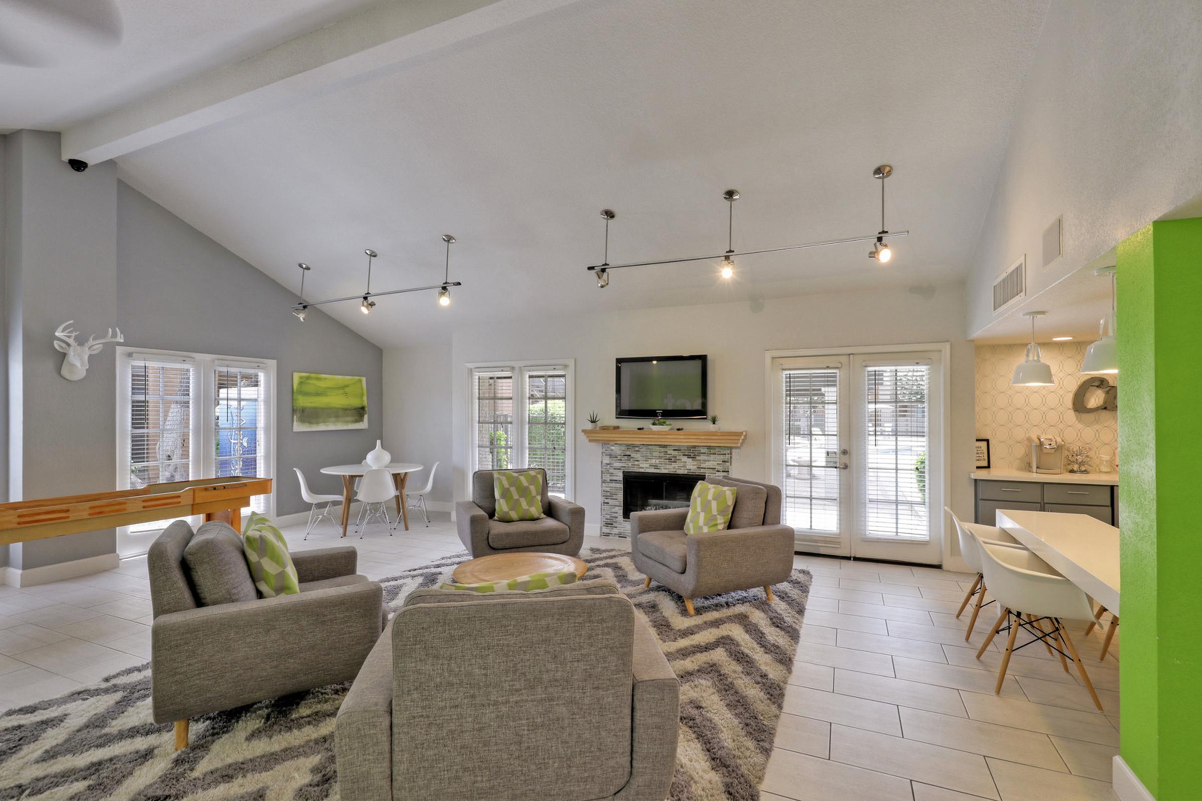 A spacious living area featuring four gray armchairs with green accents, a circular coffee table, and a rug with zigzag patterns.