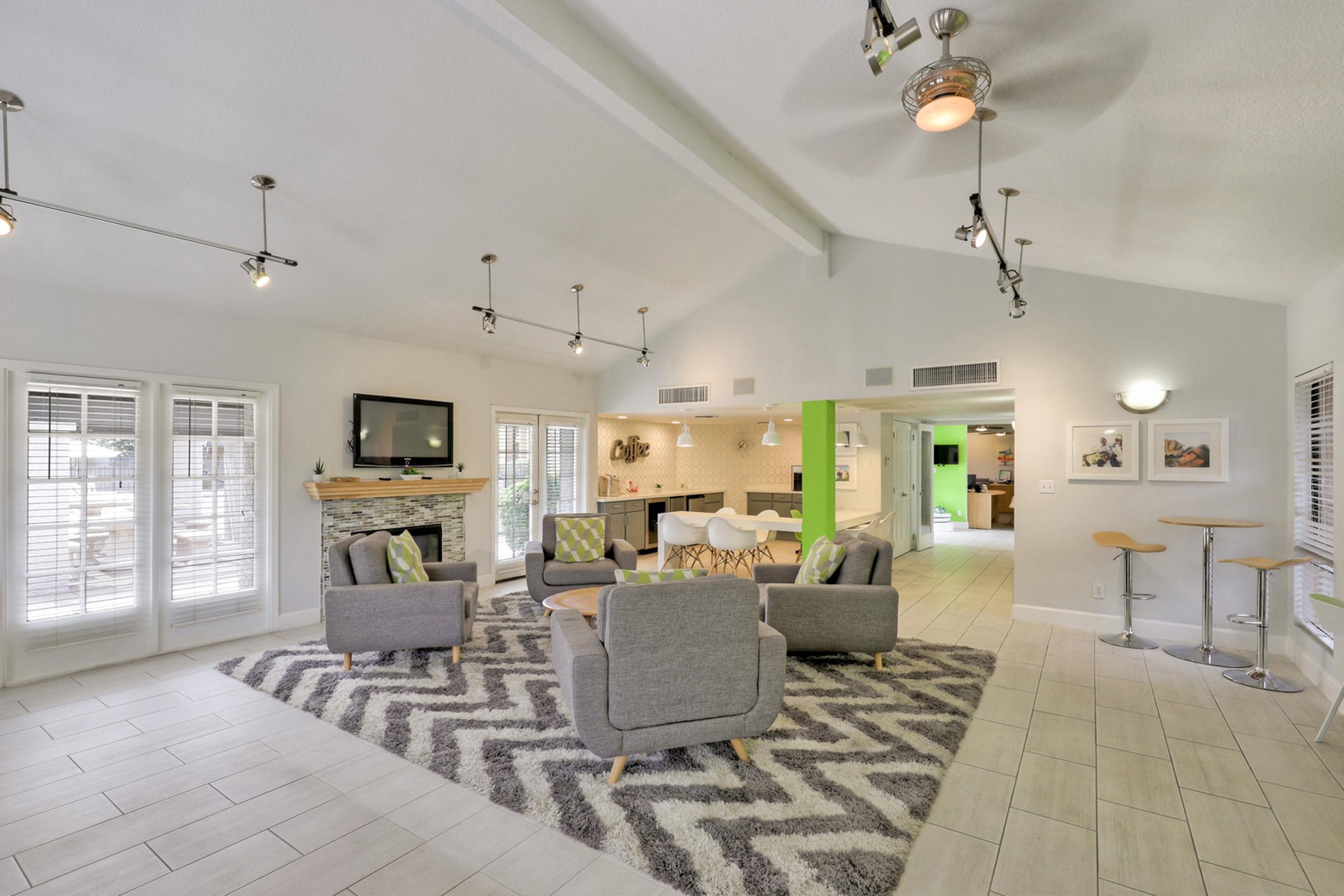 A modern living room featuring a light color scheme with gray and white tones. It includes comfortable seating, a fireplace, and decorative lighting.